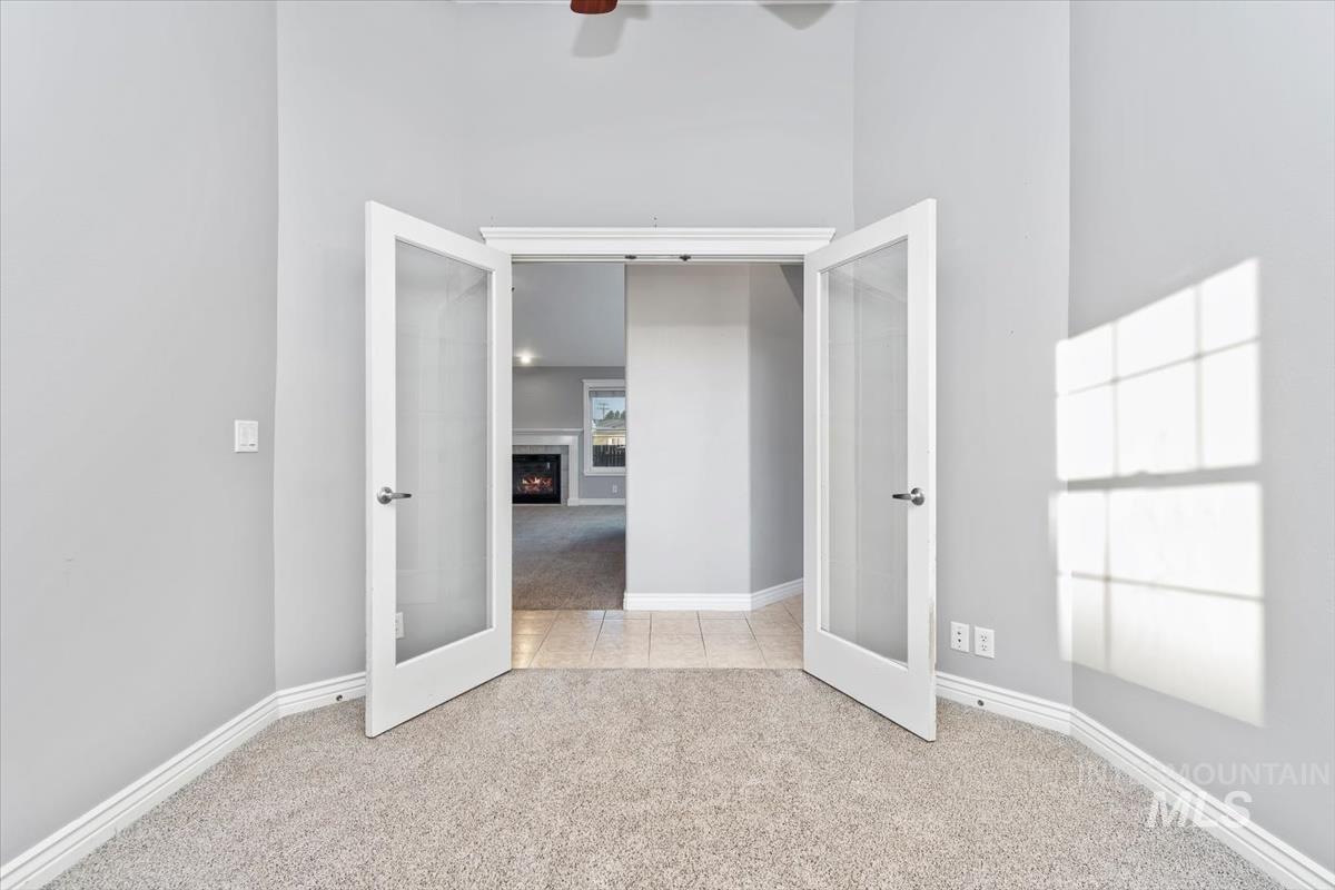Unfurnished bedroom with light carpet, french doors, a lit fireplace, and a high ceiling