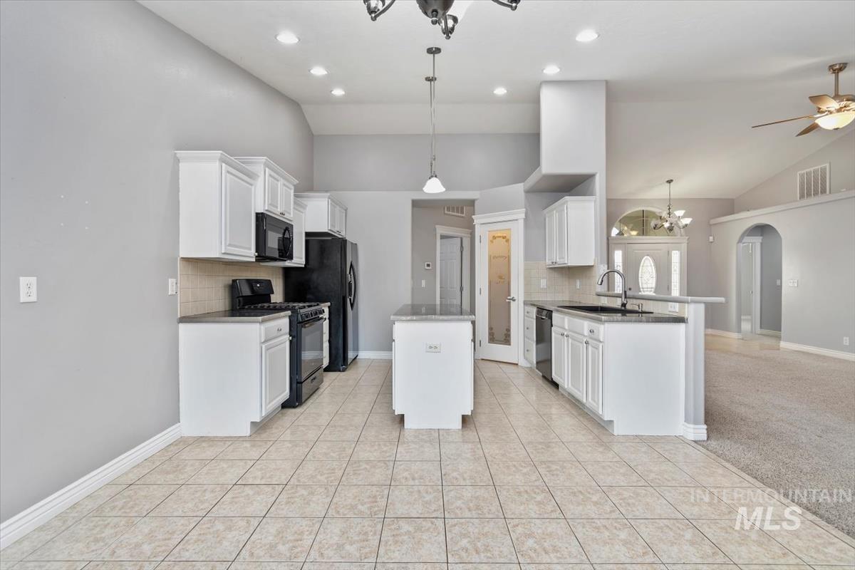 Kitchen with lofted ceiling, white cabinets, black appliances, arched walkways, and a peninsula