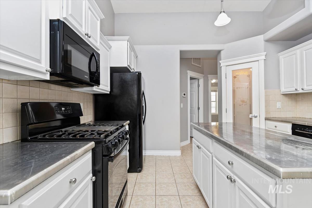 Kitchen with black appliances, tasteful backsplash, white cabinetry, hanging light fixtures, and light tile patterned floors