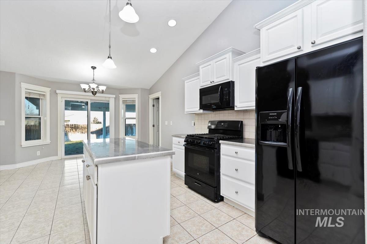 Kitchen featuring black appliances, tasteful backsplash, lofted ceiling, pendant lighting, and white cabinets