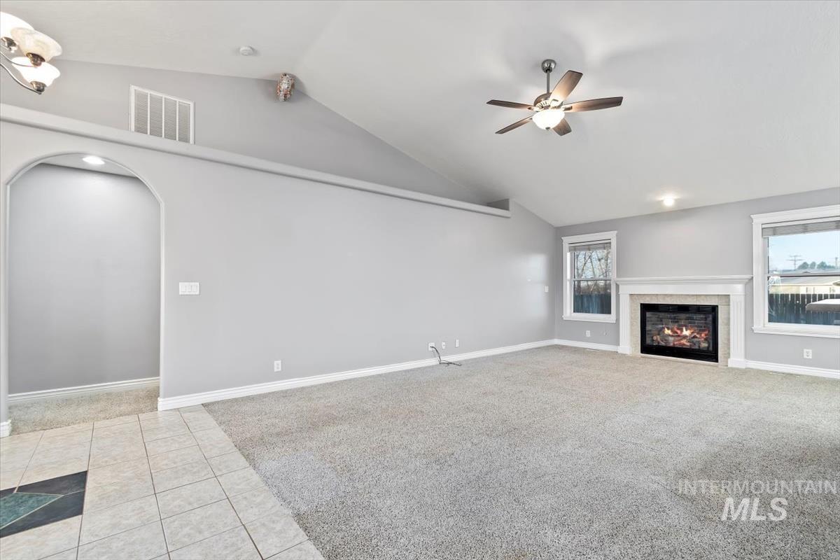 Unfurnished living room with vaulted ceiling, light colored carpet, light tile patterned flooring, arched walkways, and a tiled fireplace