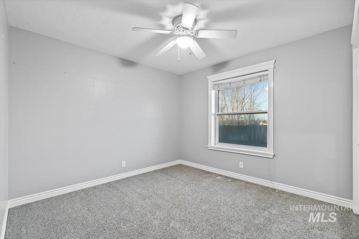 Carpeted empty room featuring a ceiling fan and baseboards