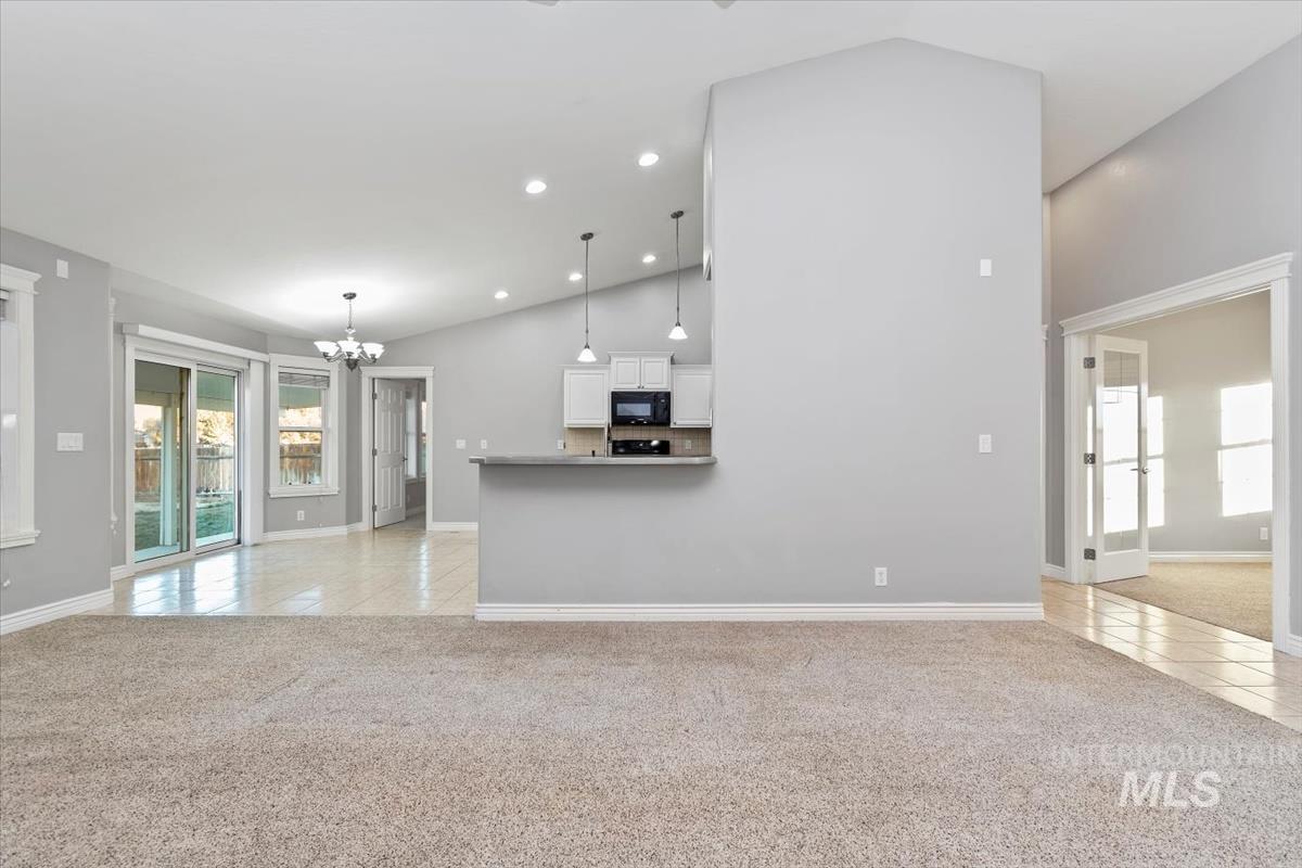 Unfurnished living room featuring light carpet, light tile patterned floors, a chandelier, recessed lighting, and lofted ceiling