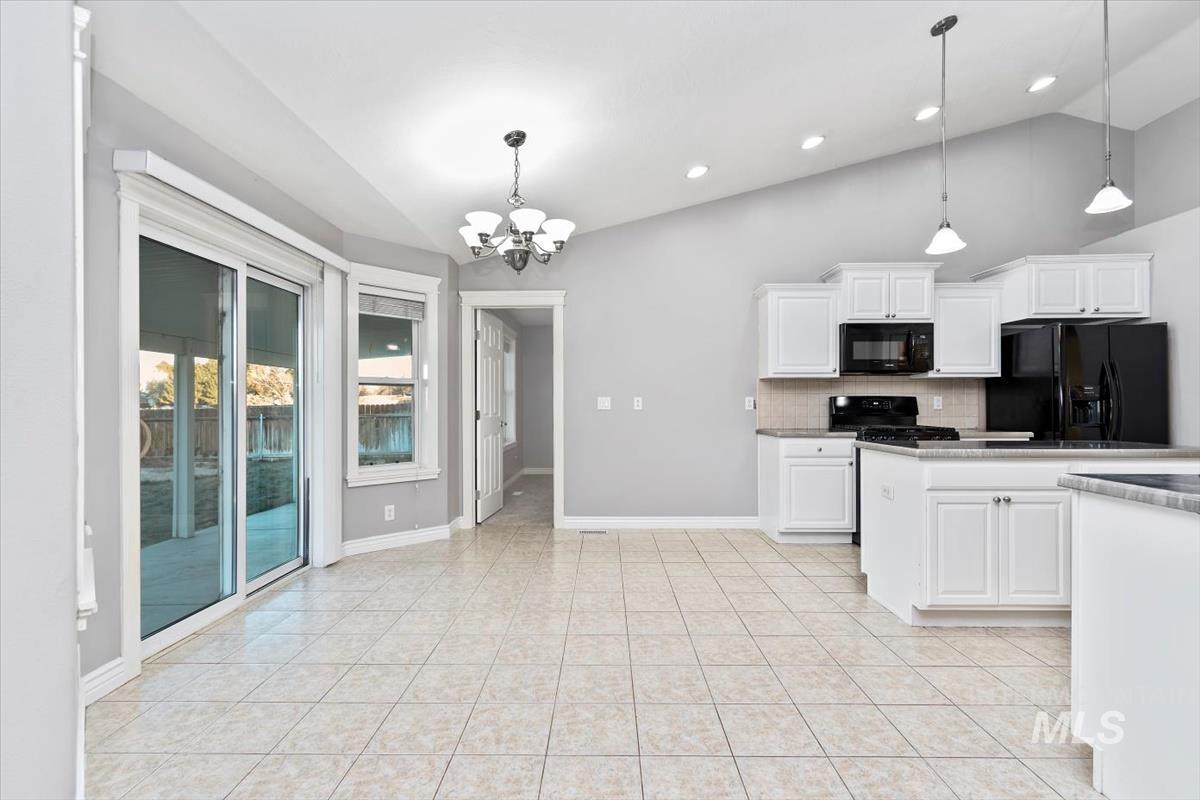 Kitchen with lofted ceiling, white cabinetry, black appliances, backsplash, and a chandelier