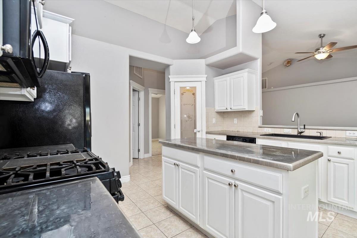 Kitchen featuring white cabinets, vaulted ceiling, black appliances, pendant lighting, and decorative backsplash