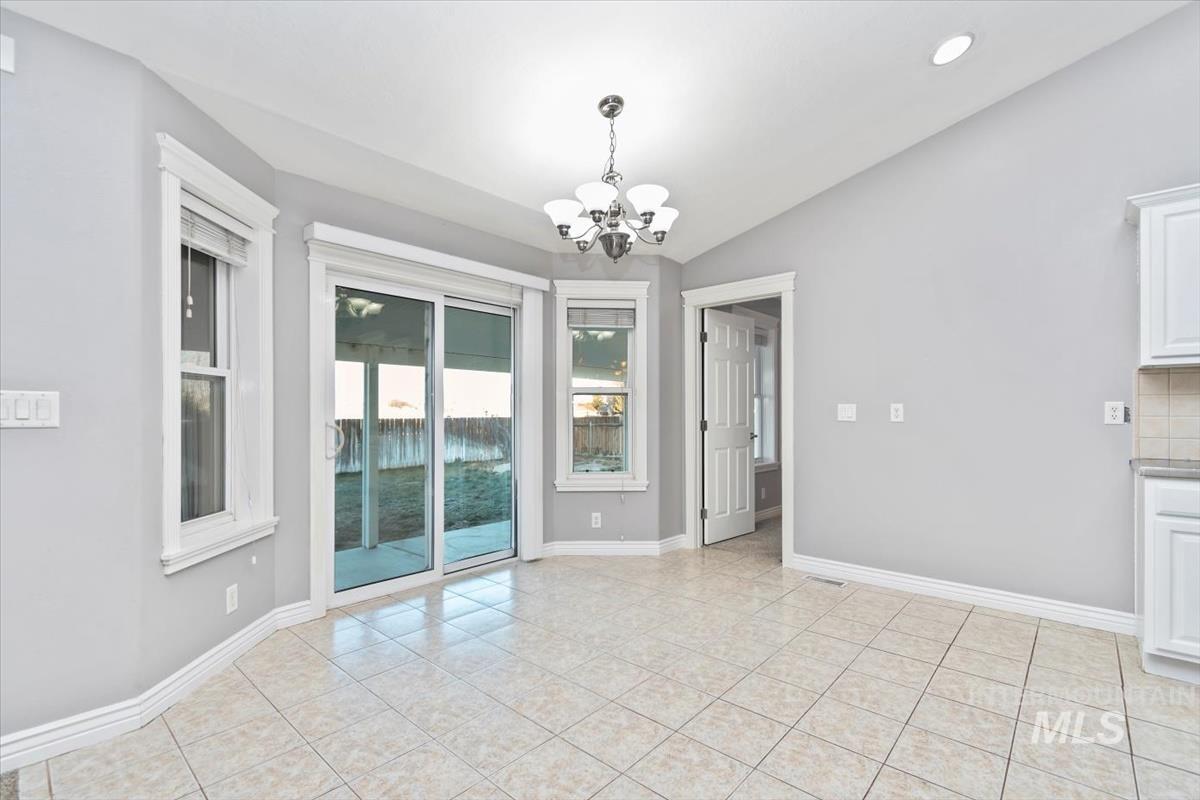Unfurnished dining area featuring a chandelier, vaulted ceiling, and light tile patterned flooring