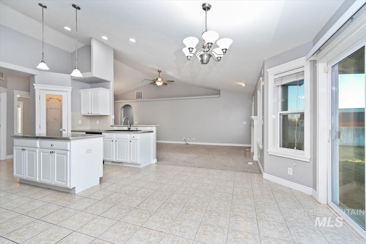 Kitchen with lofted ceiling, white cabinets, a chandelier, decorative light fixtures, and ceiling fan