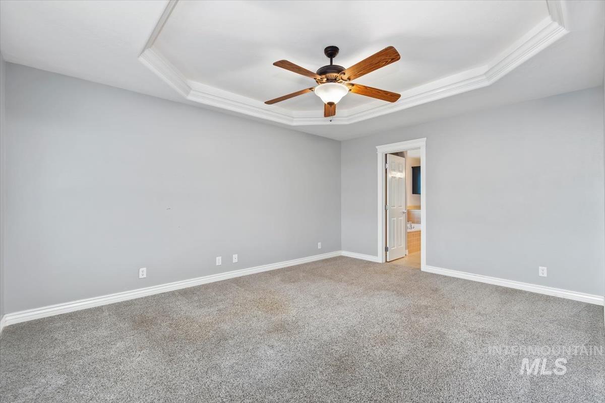 Unfurnished room with a raised ceiling, light colored carpet, and ceiling fan