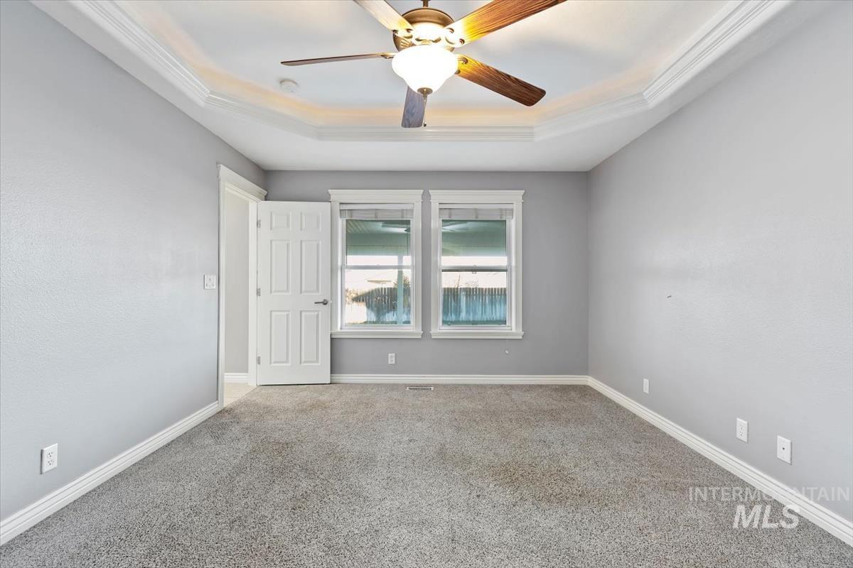 Empty room featuring a tray ceiling, carpet floors, ceiling fan, and ornamental molding