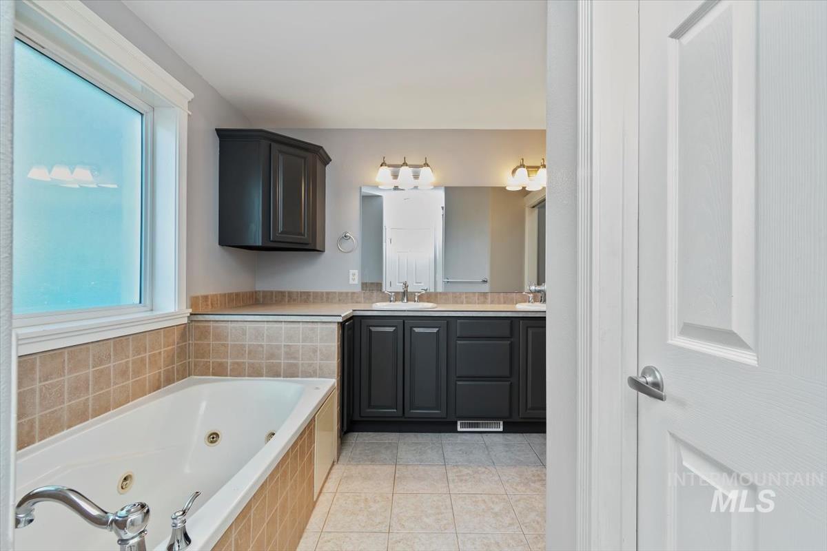 Bathroom with double vanity, light tile patterned floors, and a jetted tub
