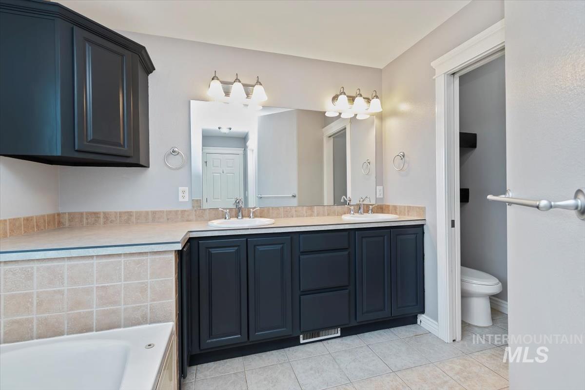 Bathroom with double vanity, light tile patterned floors, and a bath