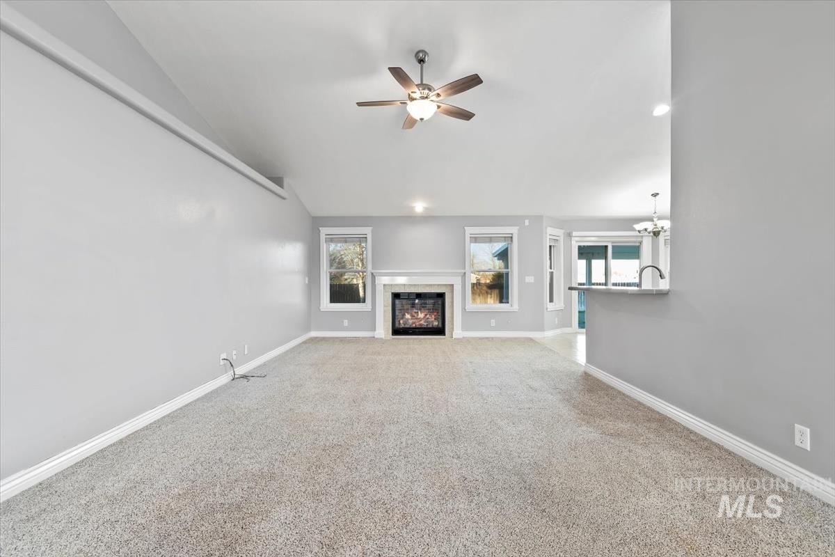 Unfurnished living room with lofted ceiling, a tiled fireplace, ceiling fan, light carpet, and a chandelier