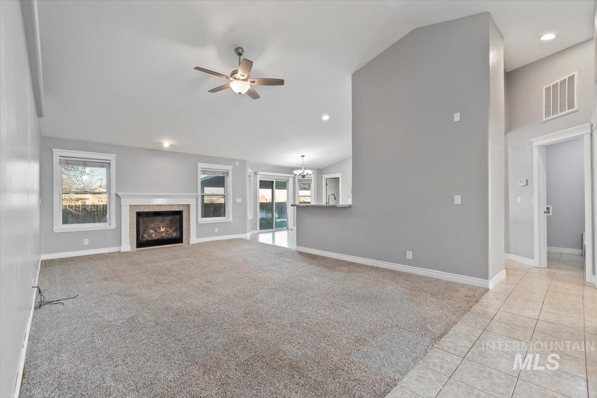 Unfurnished living room with vaulted ceiling, recessed lighting, light carpet, a tile fireplace, and a ceiling fan
