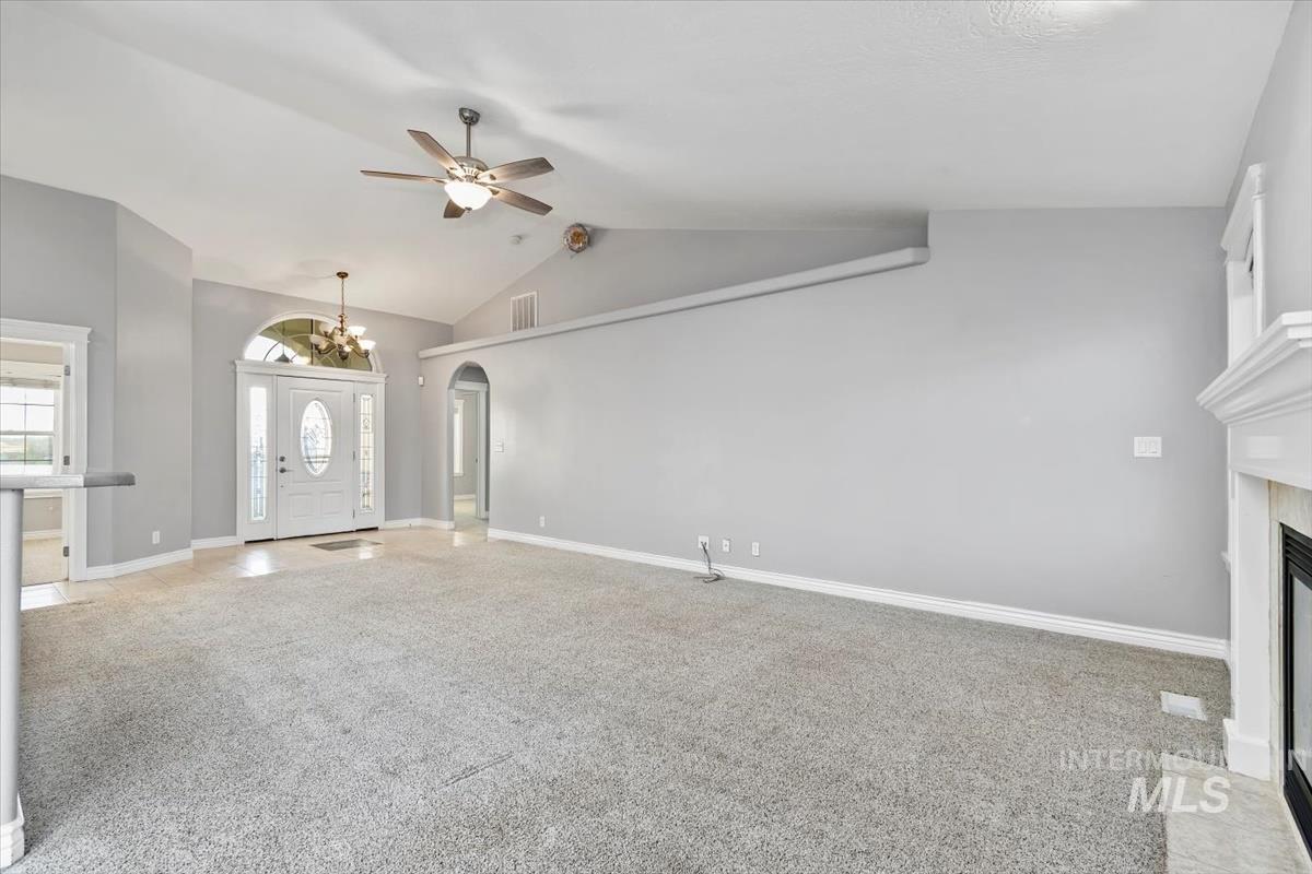 Unfurnished living room featuring light carpet, arched walkways, lofted ceiling, a fireplace, and a chandelier
