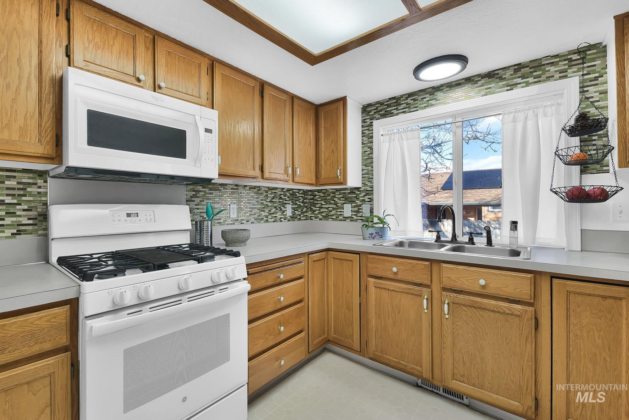 Kitchen with white appliances, brown cabinetry, light countertops, light flooring, and tasteful backsplash