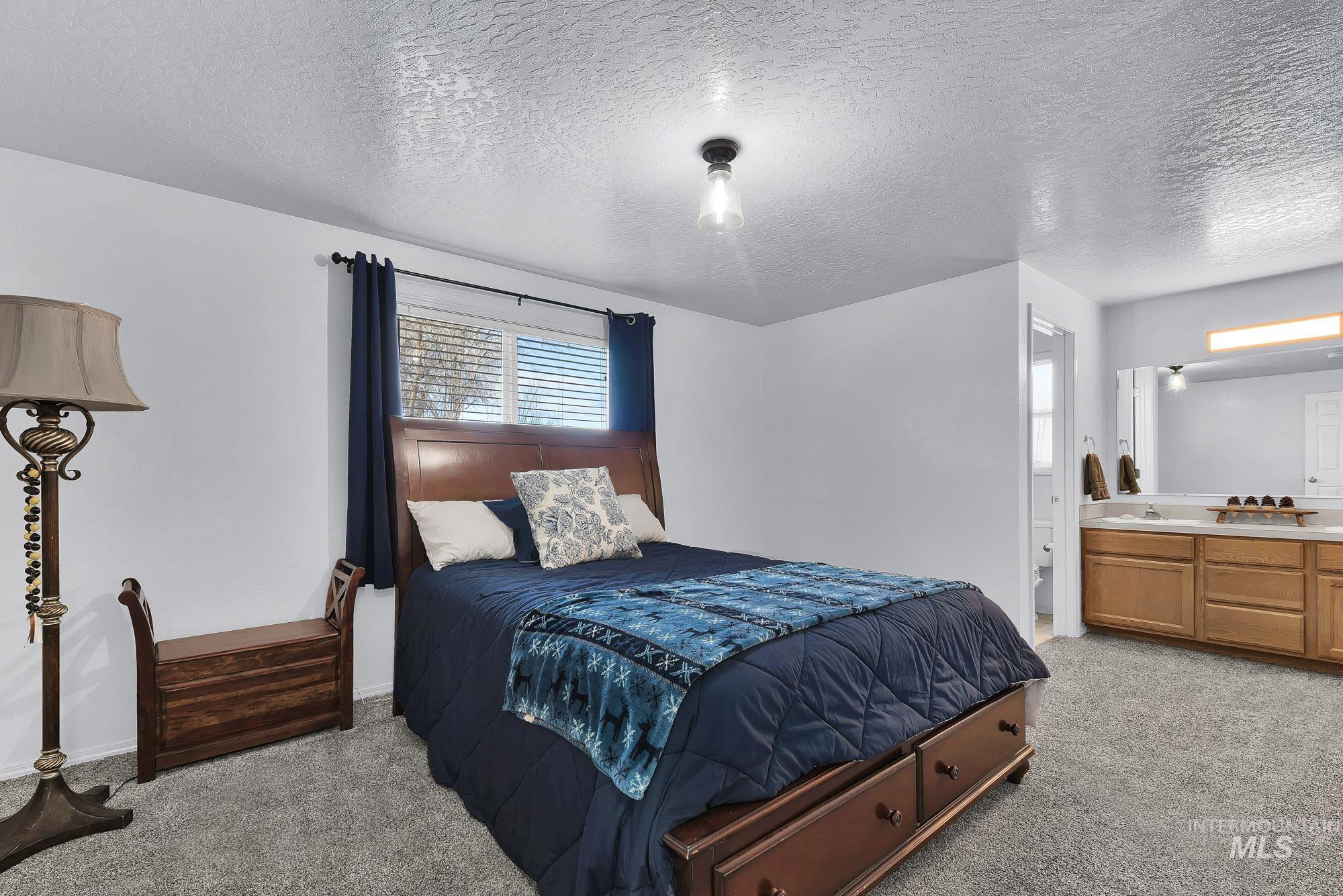 Bedroom with a textured ceiling, light carpet, and ensuite bath