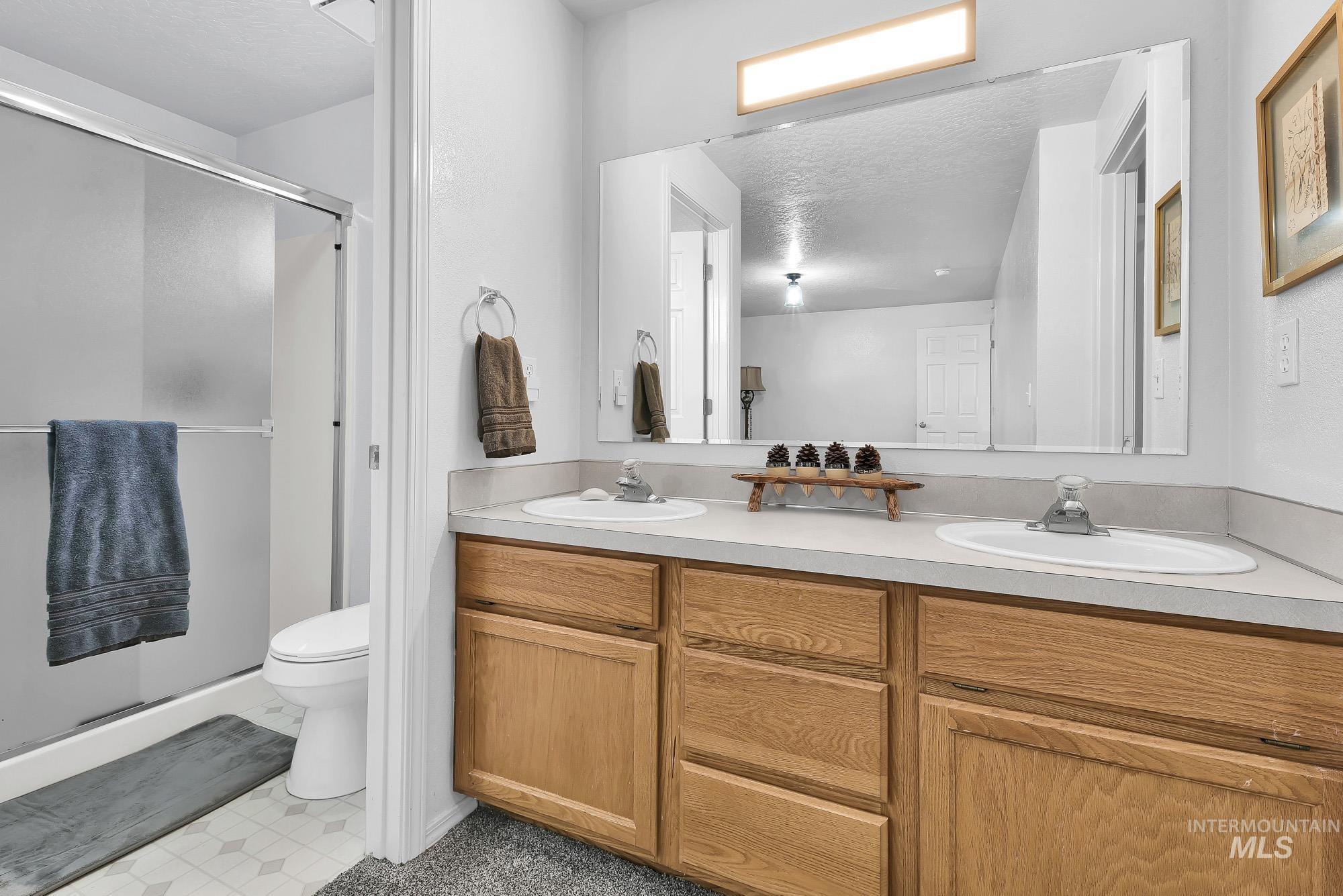Full bath with double vanity, a stall shower, a textured ceiling, and light floors