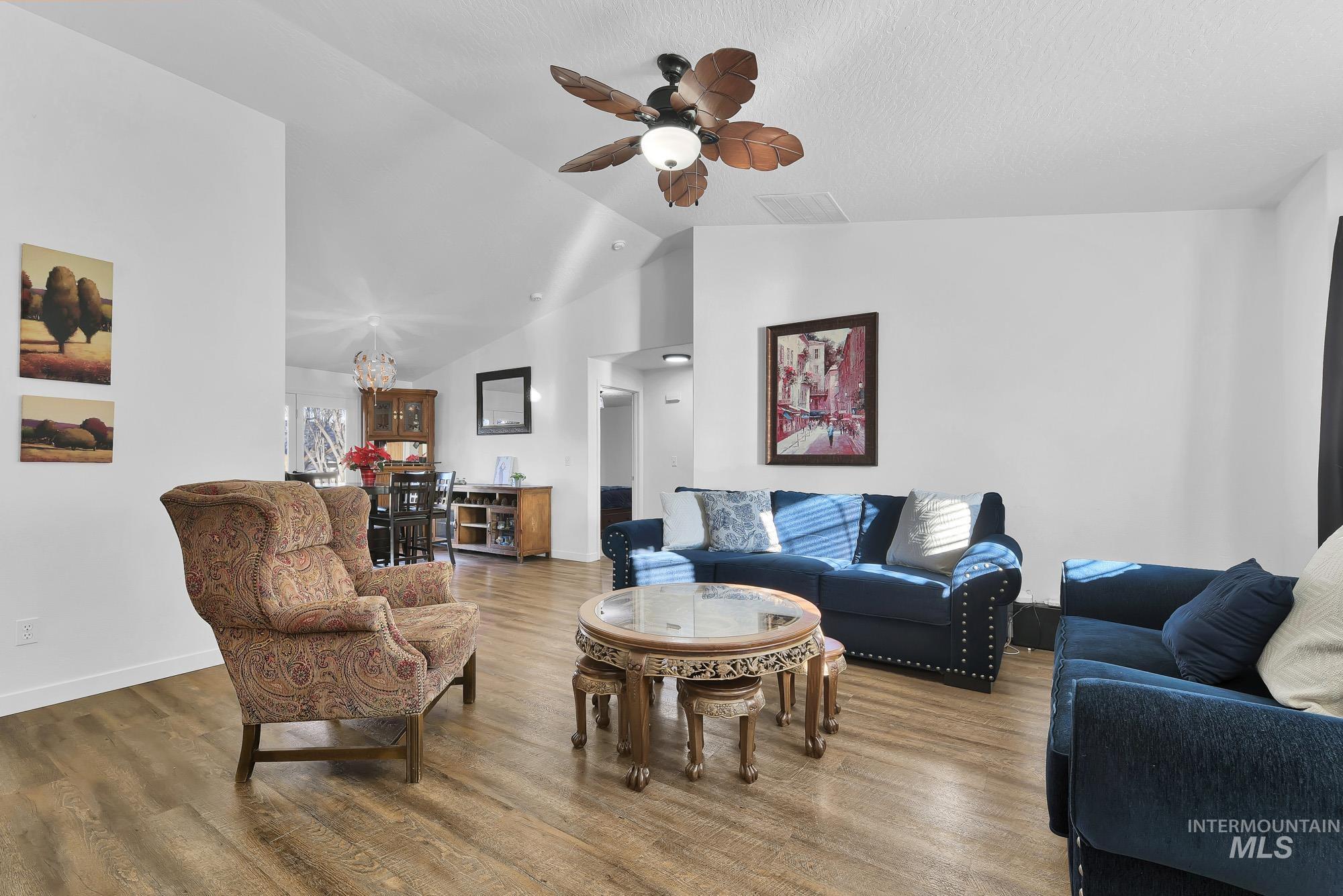 Living room featuring wood finished floors, lofted ceiling, ceiling fan, and a chandelier