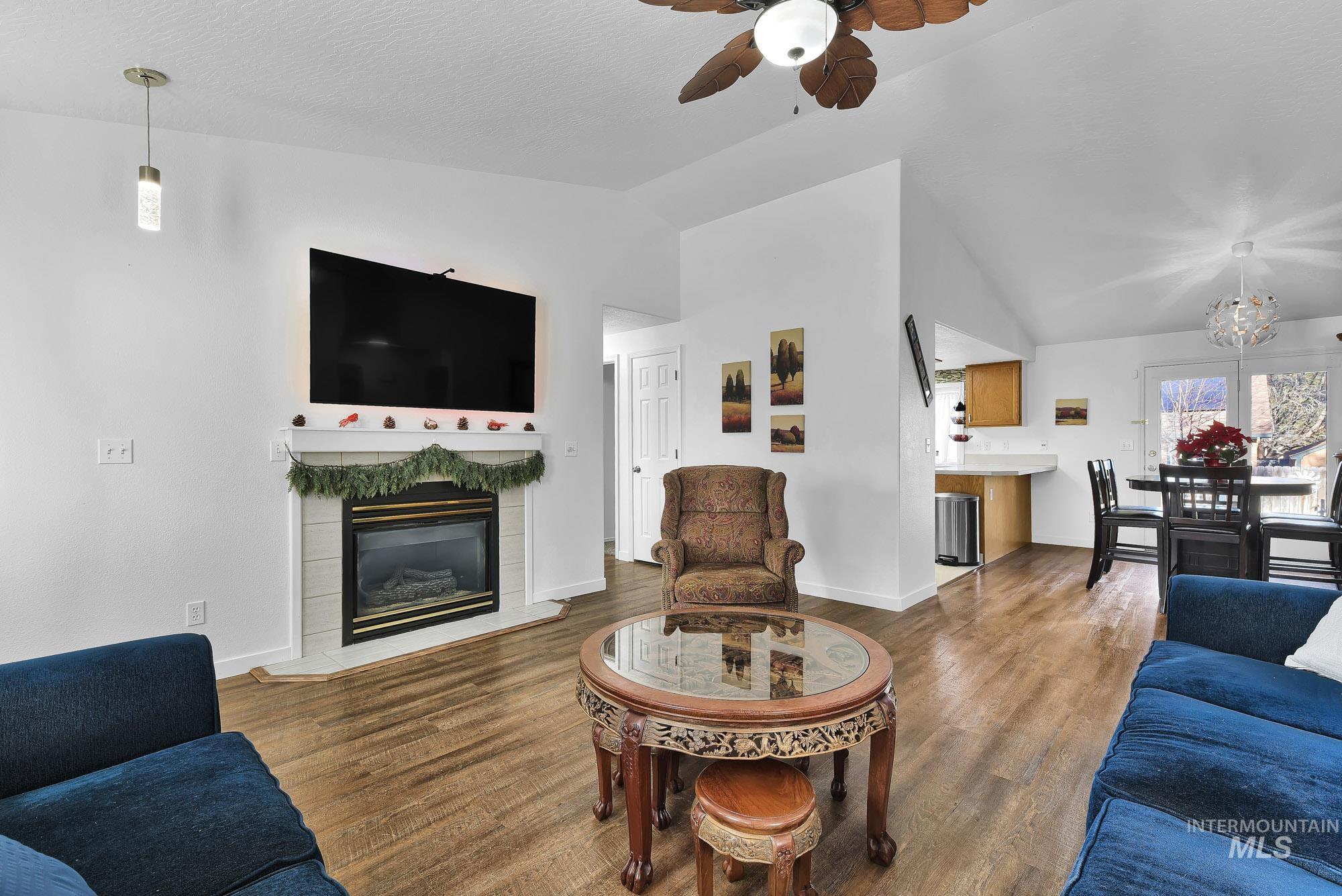 Living area featuring vaulted ceiling, ceiling fan, dark wood-style flooring, a tiled fireplace, and a textured ceiling