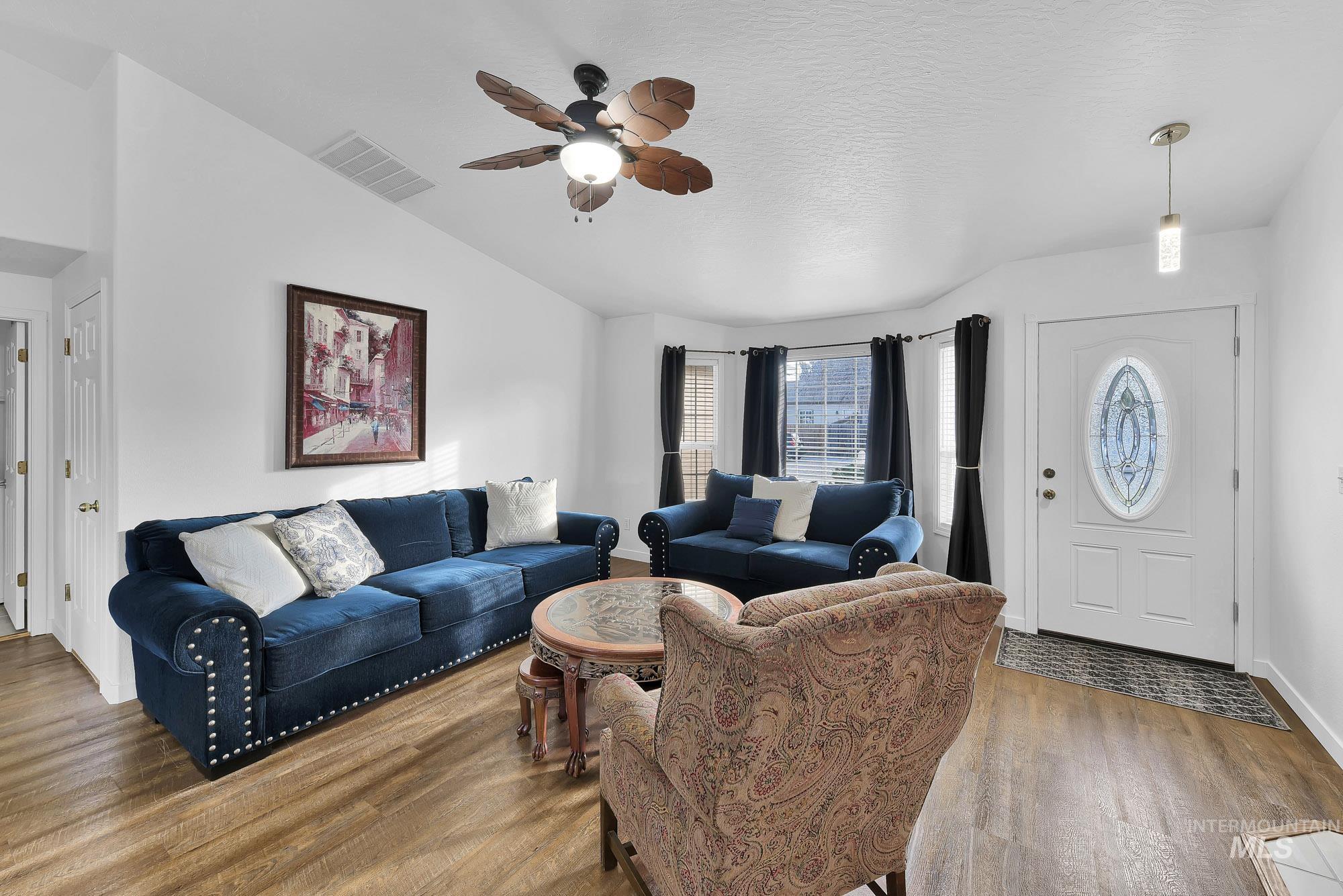 Living room featuring wood finished floors, ceiling fan, vaulted ceiling, and a textured ceiling