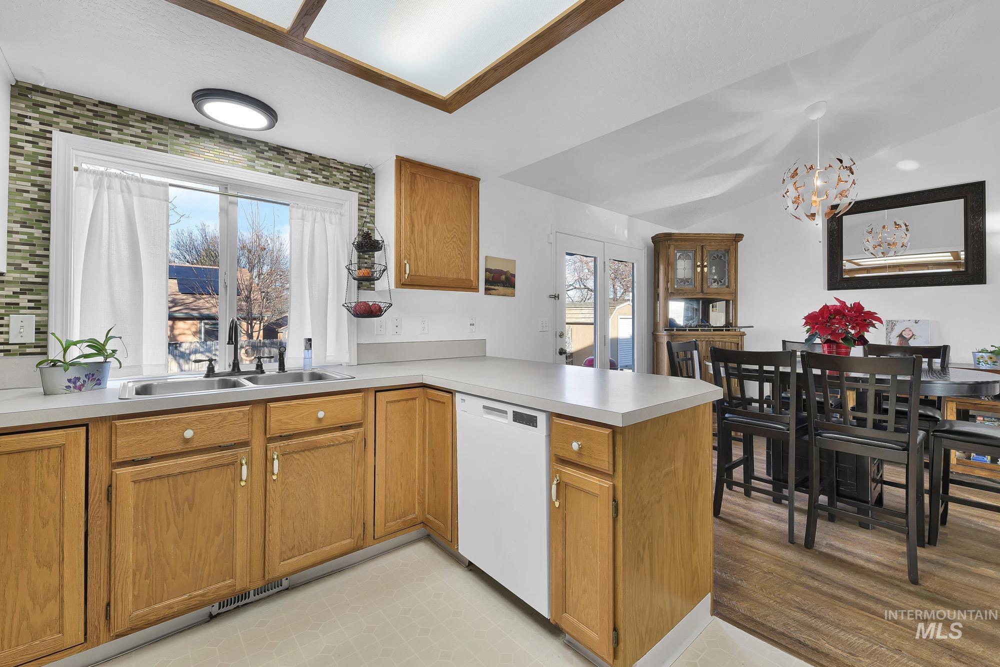 Kitchen with brown cabinets, light countertops, a peninsula, dishwasher, and lofted ceiling