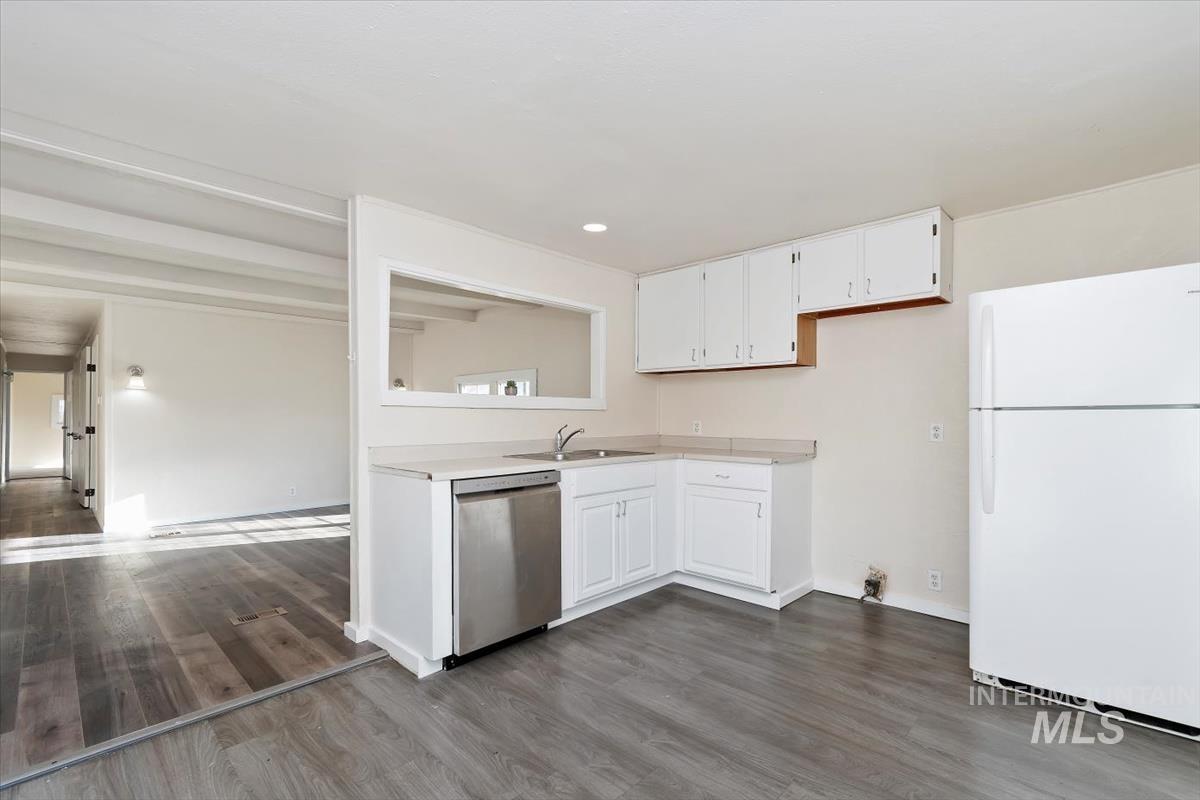 Kitchen featuring freestanding refrigerator, white cabinets, dishwasher, light countertops, and dark wood-type flooring