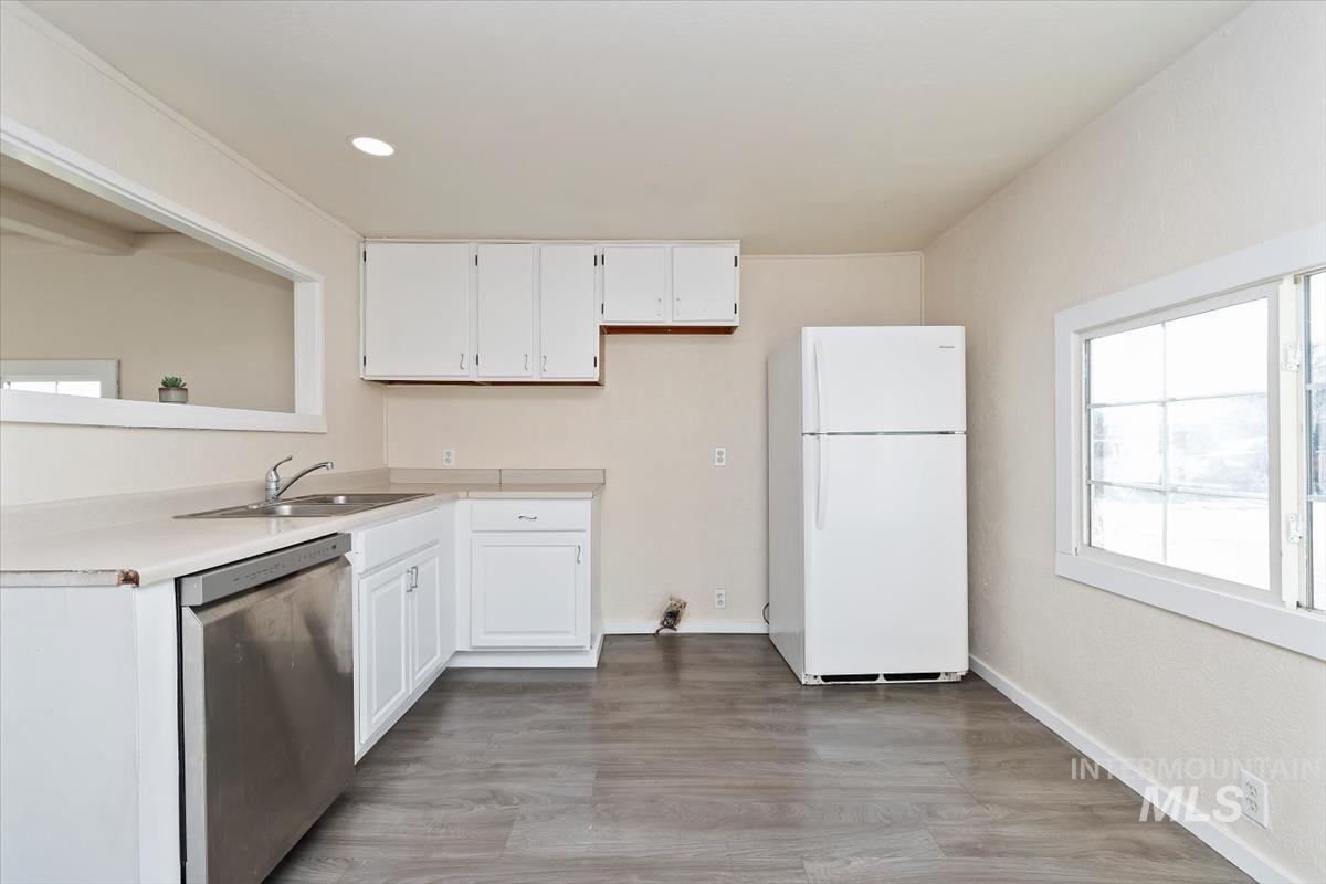 Kitchen featuring freestanding refrigerator, light countertops, dishwasher, white cabinets, and light wood-style floors