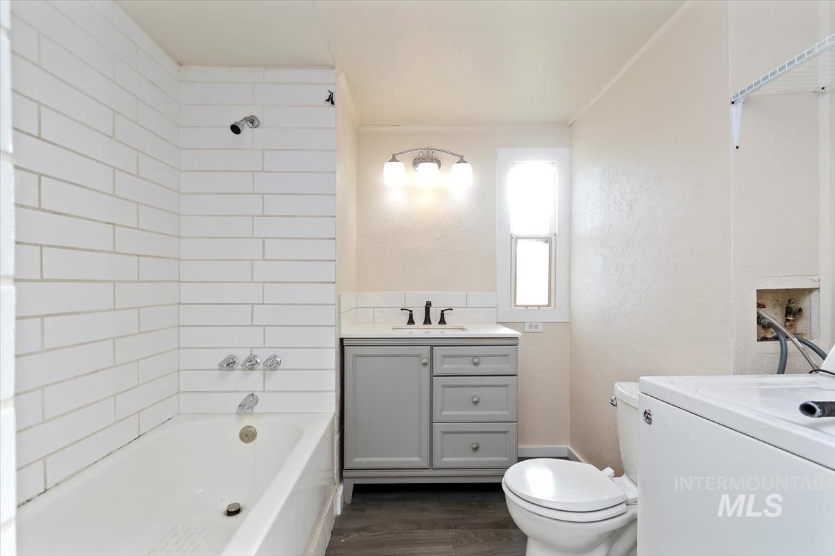 Full bath featuring vanity, washer / dryer, bathing tub / shower combination, dark wood-style flooring, and a textured wall