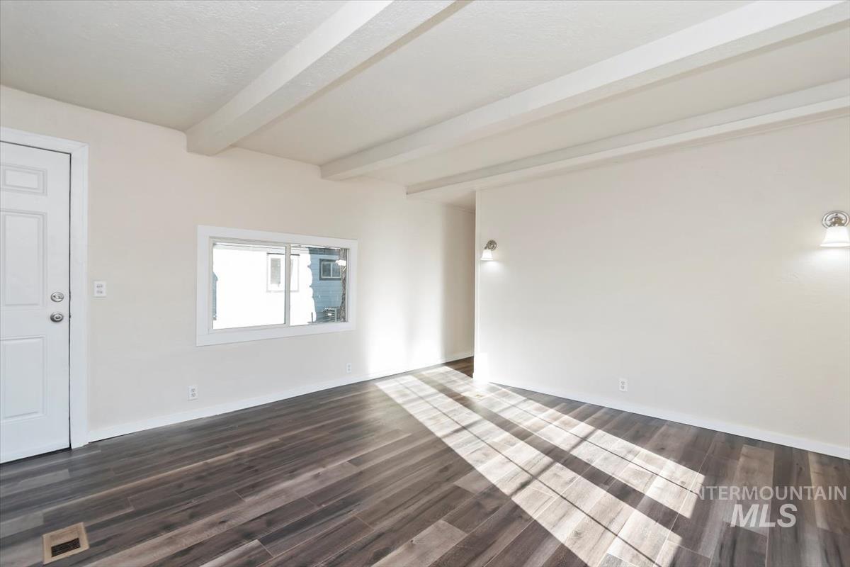 Empty room featuring dark wood-style floors and beam ceiling