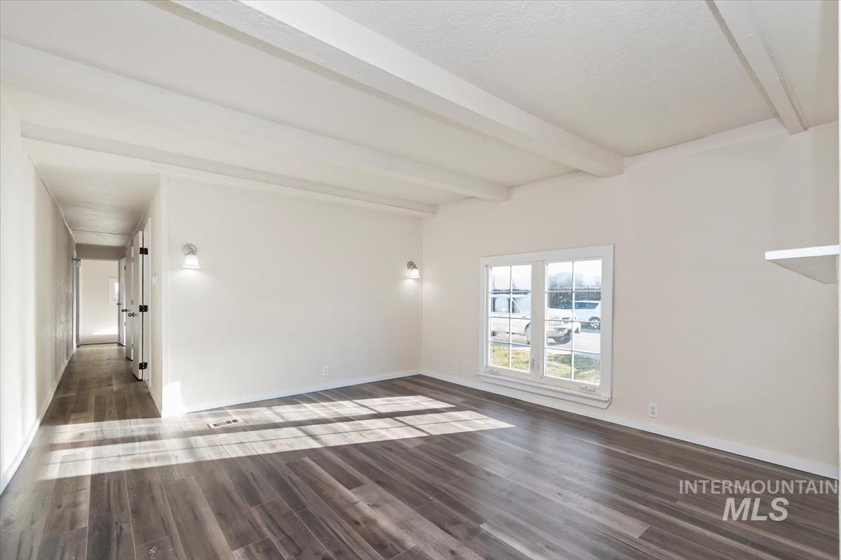 Unfurnished room with beam ceiling and dark wood-type flooring
