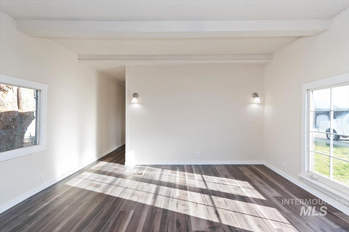 Empty room with healthy amount of natural light, beam ceiling, and dark wood-type flooring