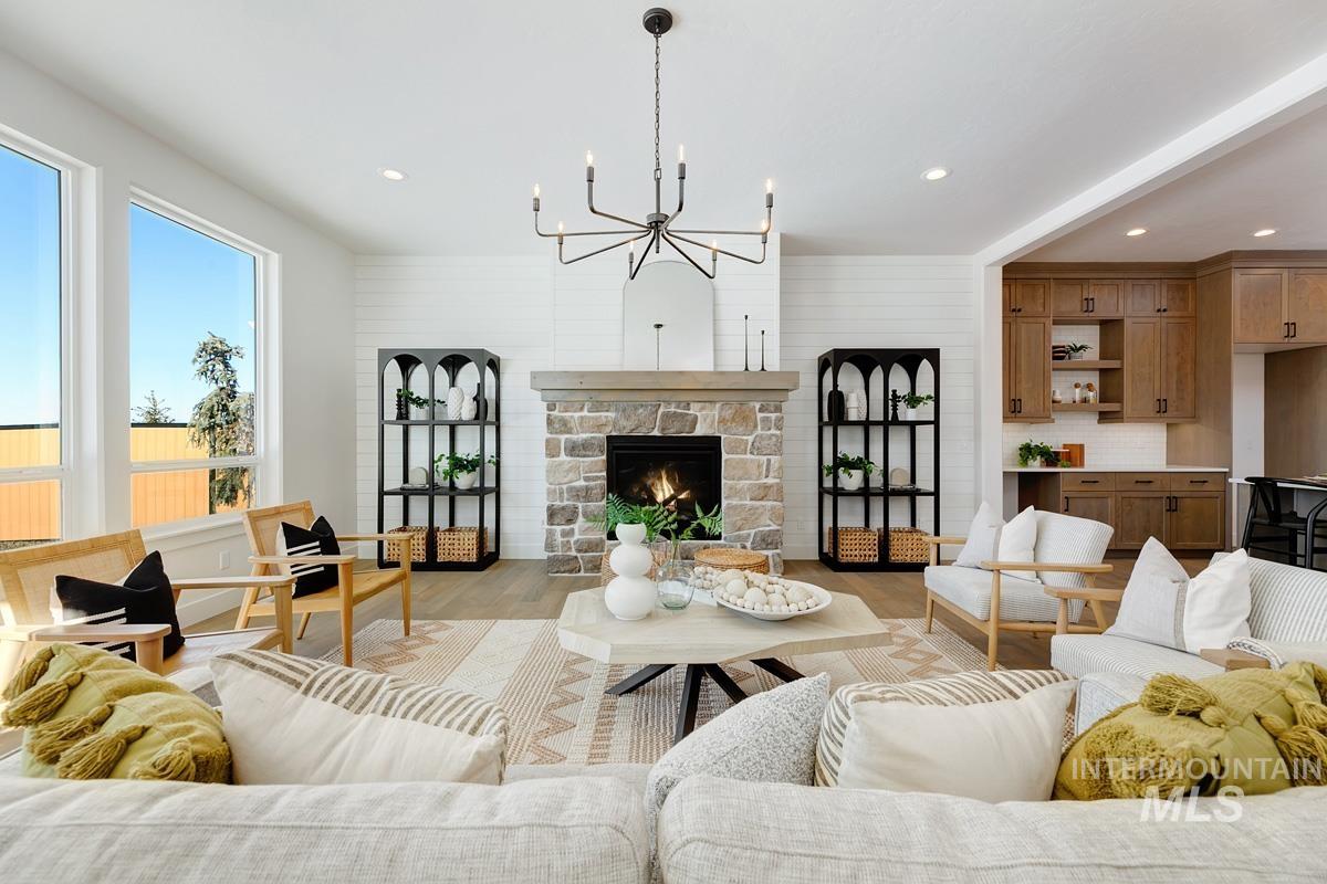 Living room with a stone fireplace, a chandelier, wood finished floors, and recessed lighting