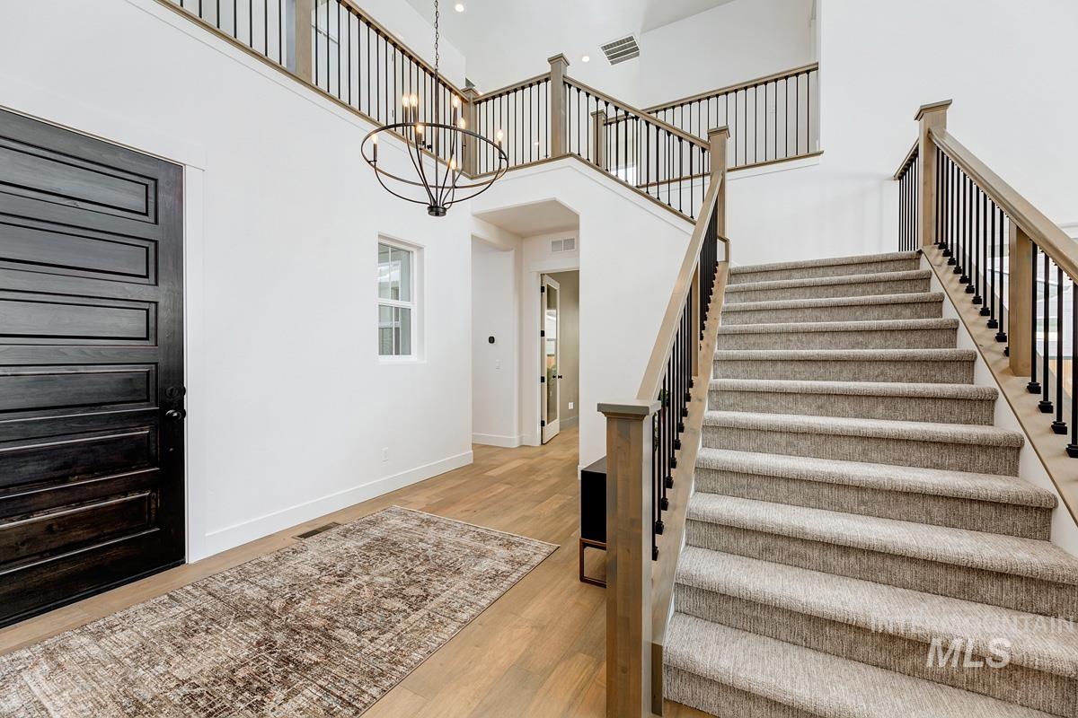 Stairs with a high ceiling, wood finished floors, and a chandelier