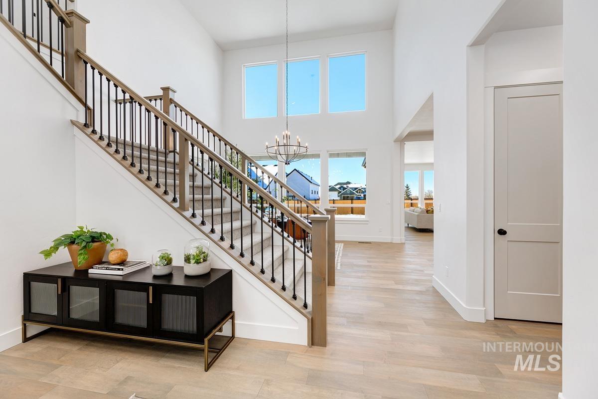 Stairs with a towering ceiling, healthy amount of natural light, a chandelier, and wood finished floors