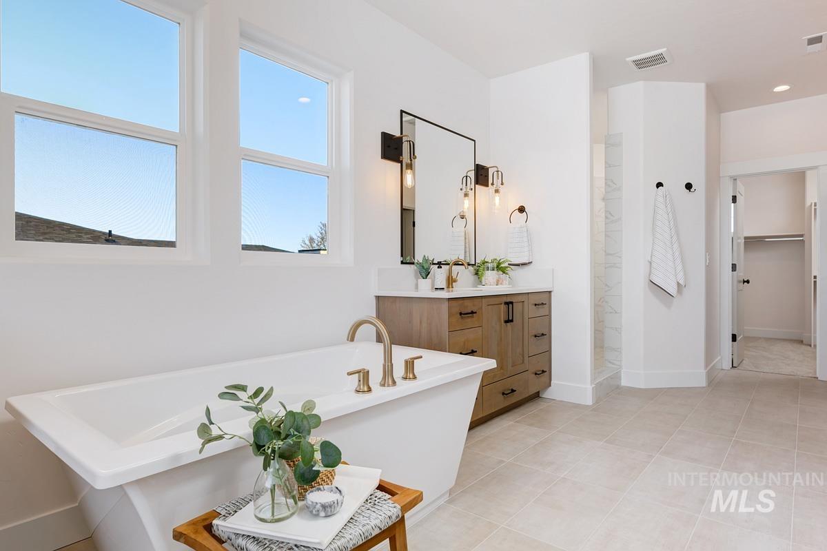 Full bathroom featuring vanity, a soaking tub, walk in shower, a spacious closet, and light tile patterned floors