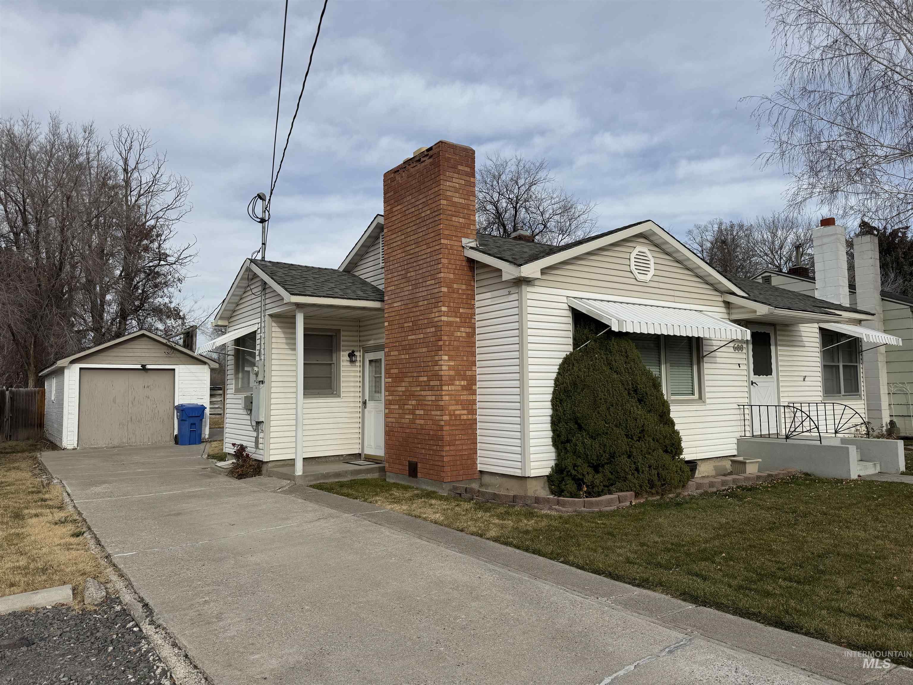View of front facade with an outdoor structure, roof with shingles, a detached garage, and a chimney
