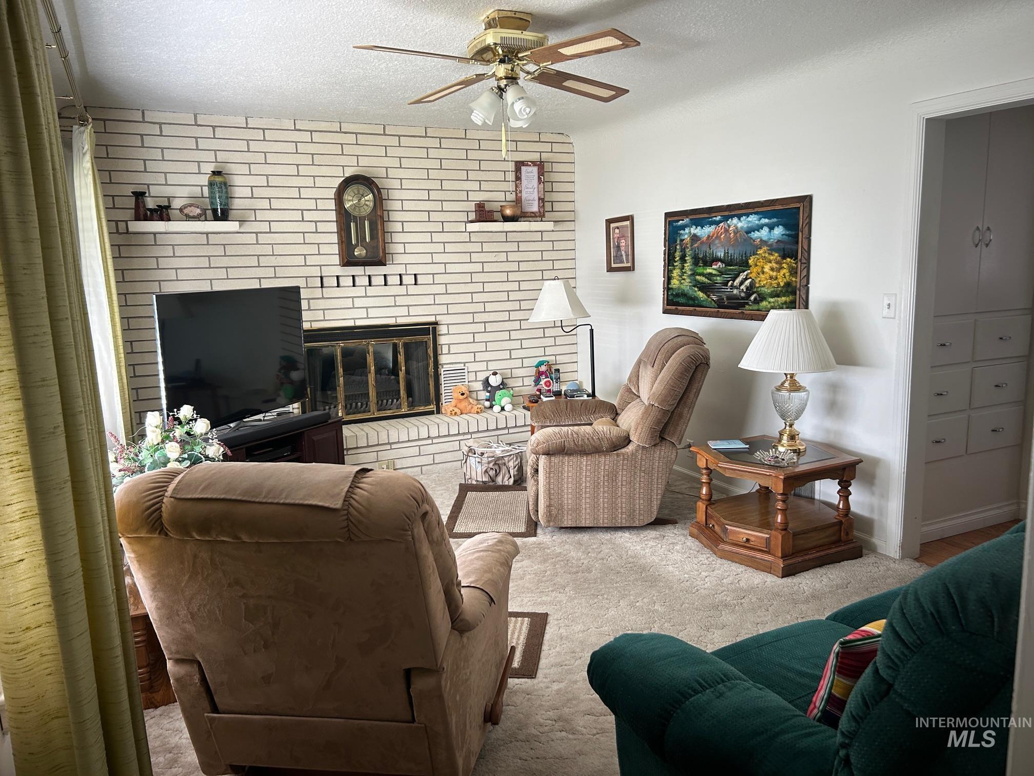 Carpeted living room with a brick fireplace, a textured ceiling, and a ceiling fan