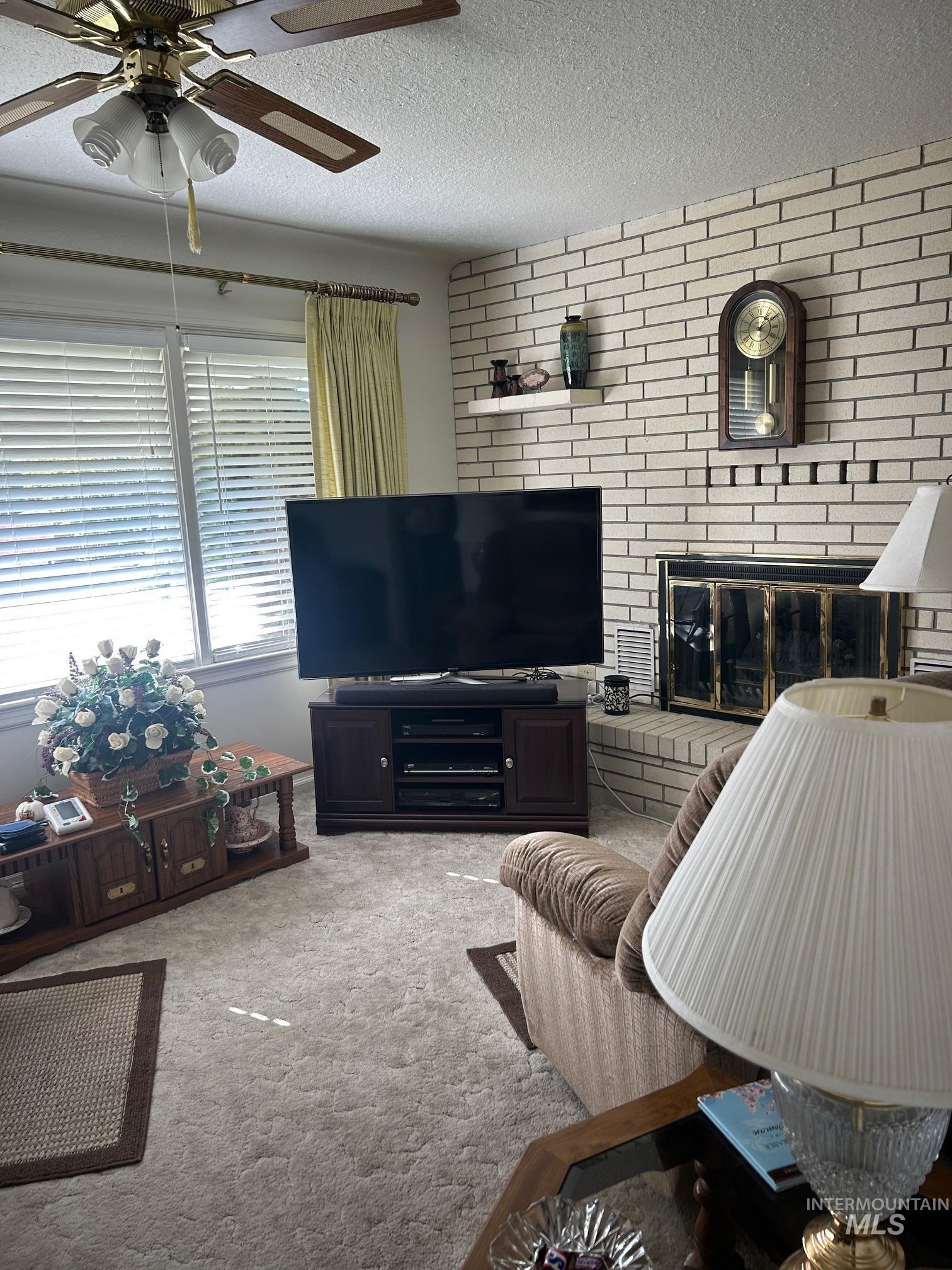Living area featuring carpet, a brick fireplace, a textured ceiling, ceiling fan, and brick wall