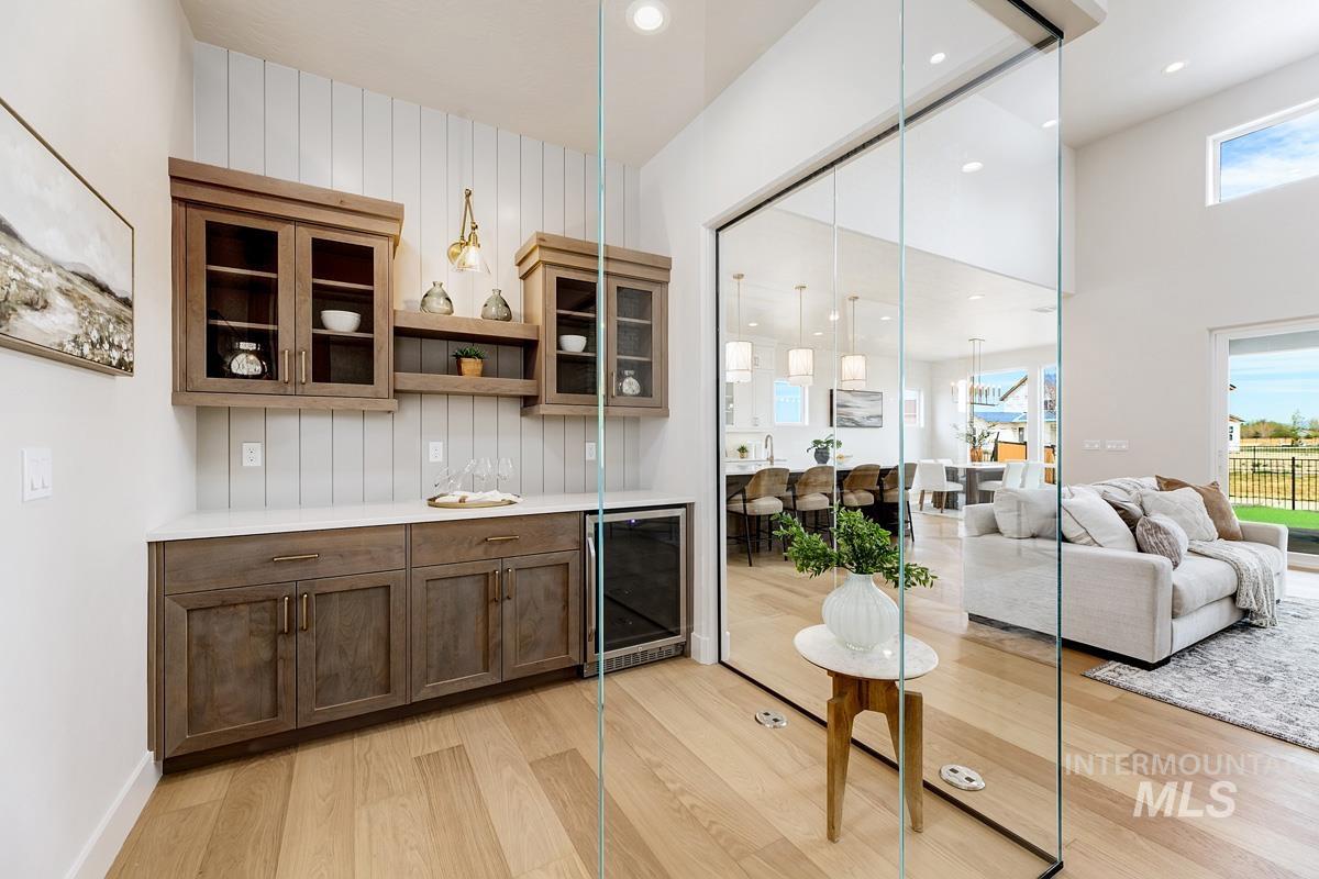 Bar featuring glass insert cabinets, open shelves, beverage cooler, hanging light fixtures, and light wood finished floors
