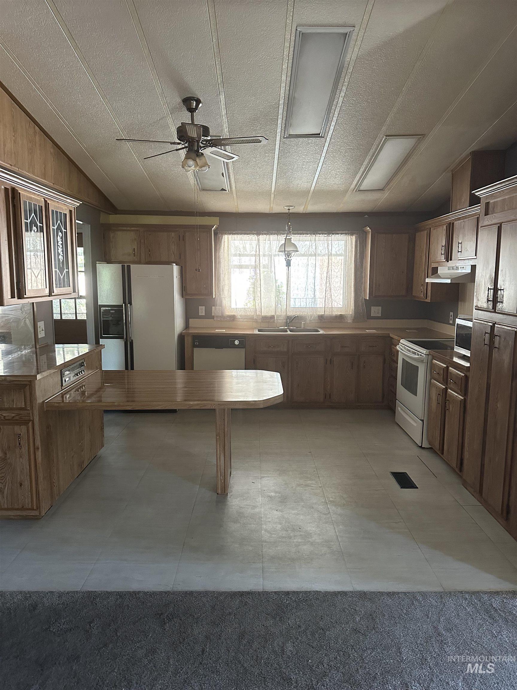 Kitchen with white appliances, ceiling fan, under cabinet range hood, a textured ceiling, and hanging light fixtures
