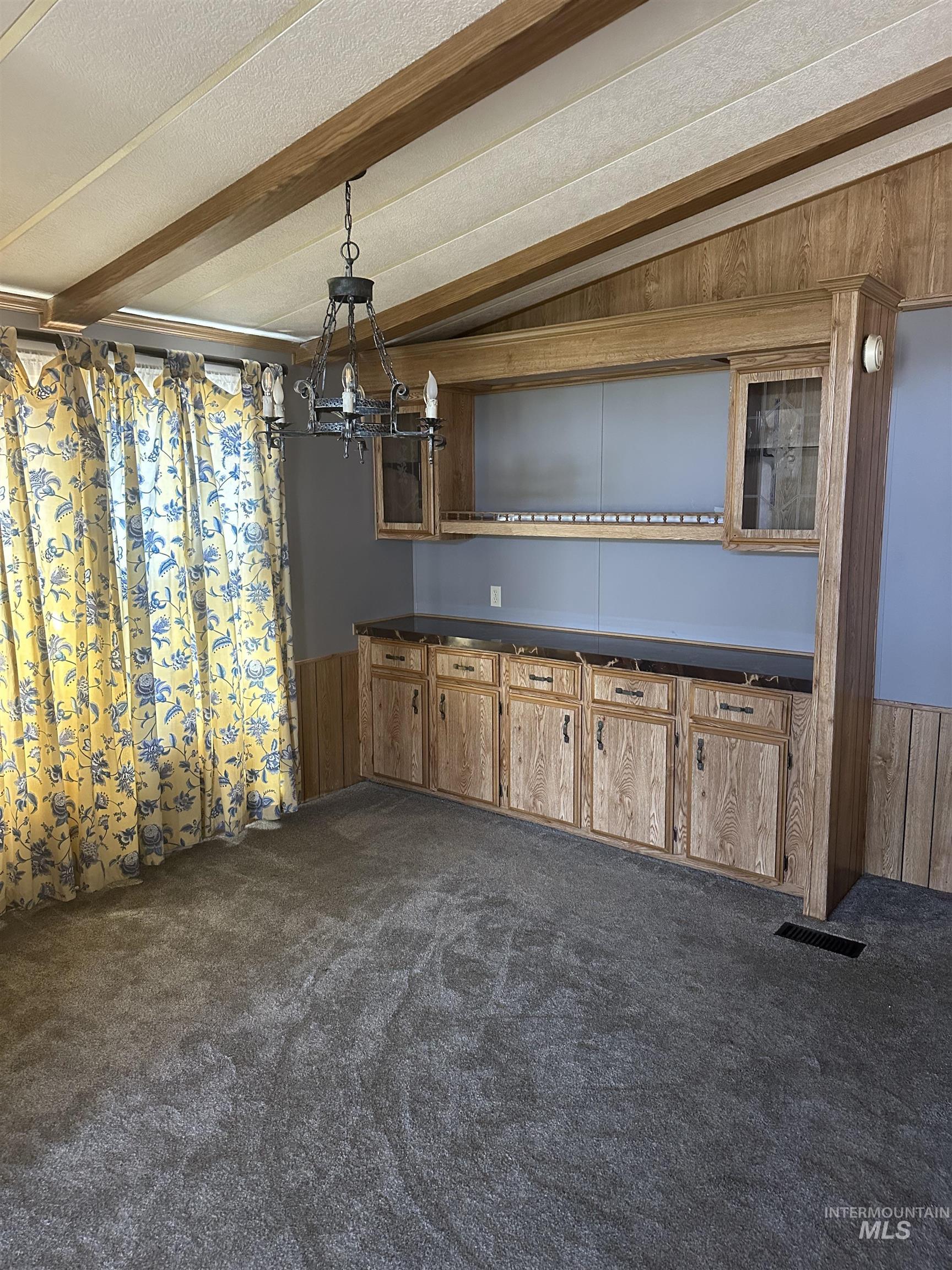 Unfurnished dining area featuring dark colored carpet, beam ceiling, wooden walls, a chandelier, and a textured ceiling