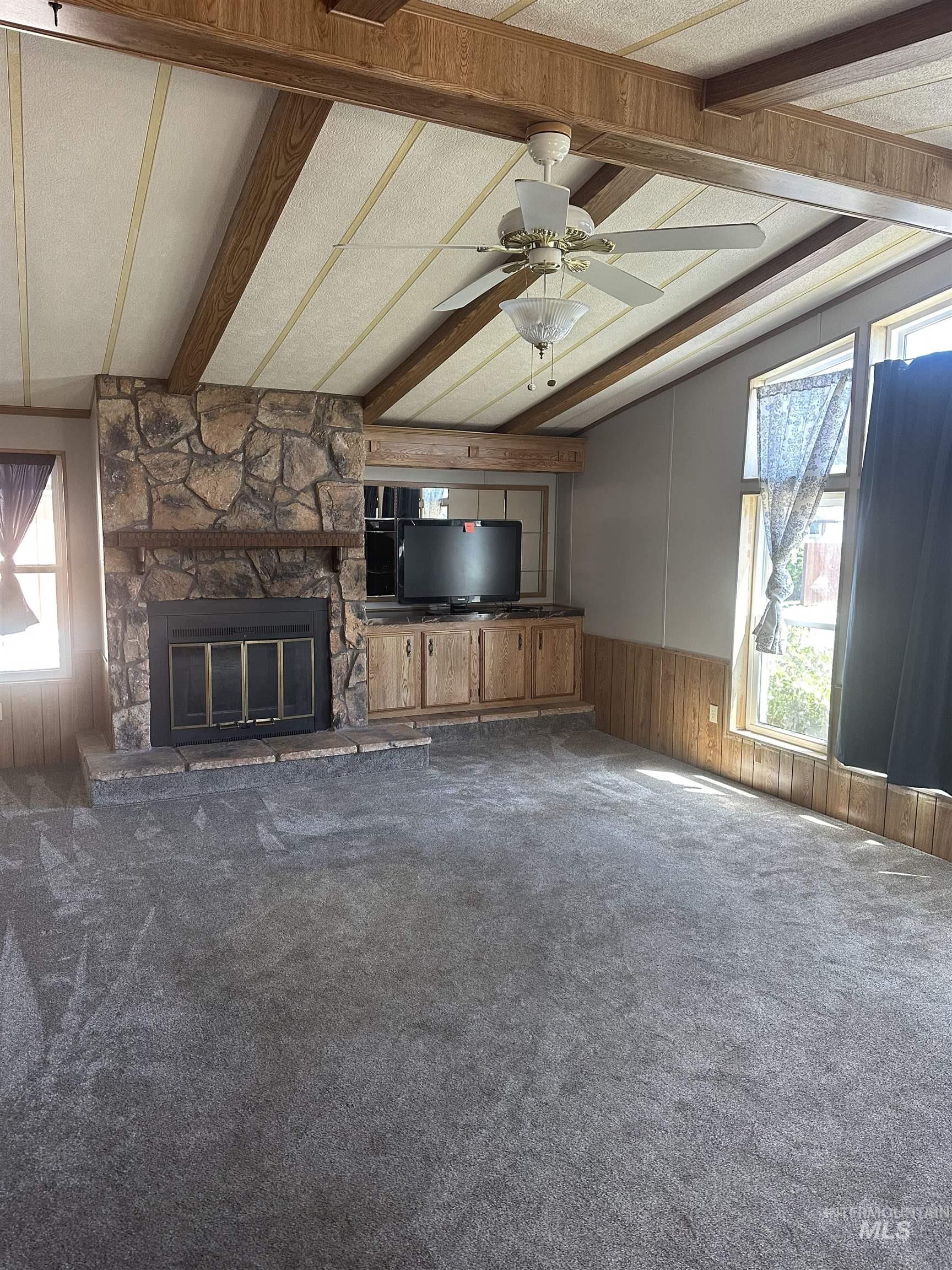 Unfurnished living room featuring carpet, wainscoting, wood walls, a stone fireplace, and ceiling fan