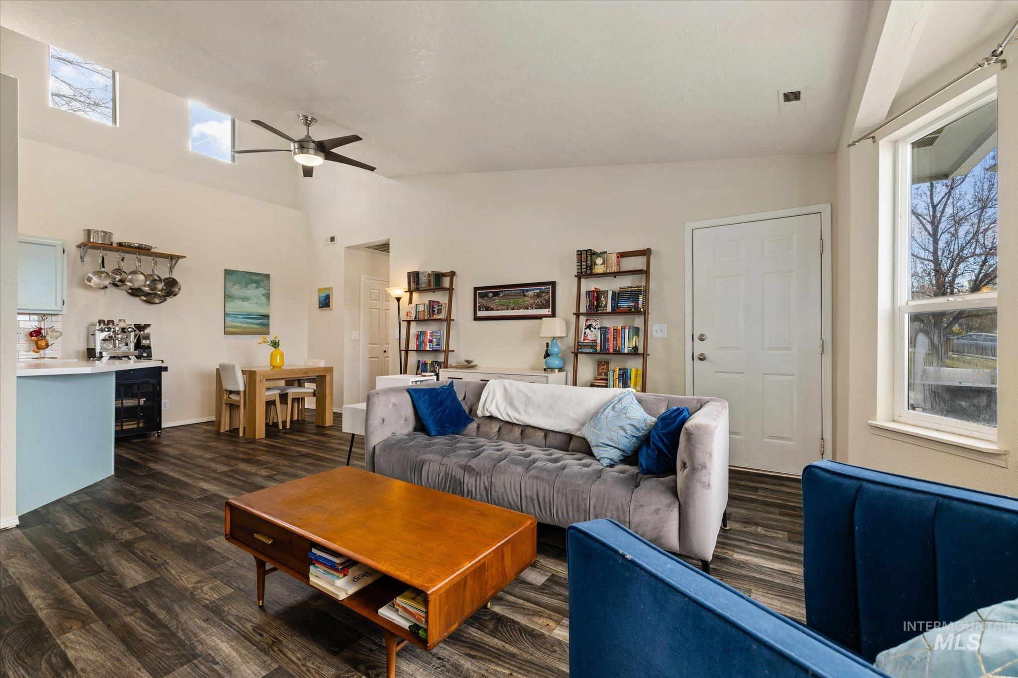 Living room featuring plenty of natural light, dark wood-style floors, ceiling fan, and high vaulted ceiling