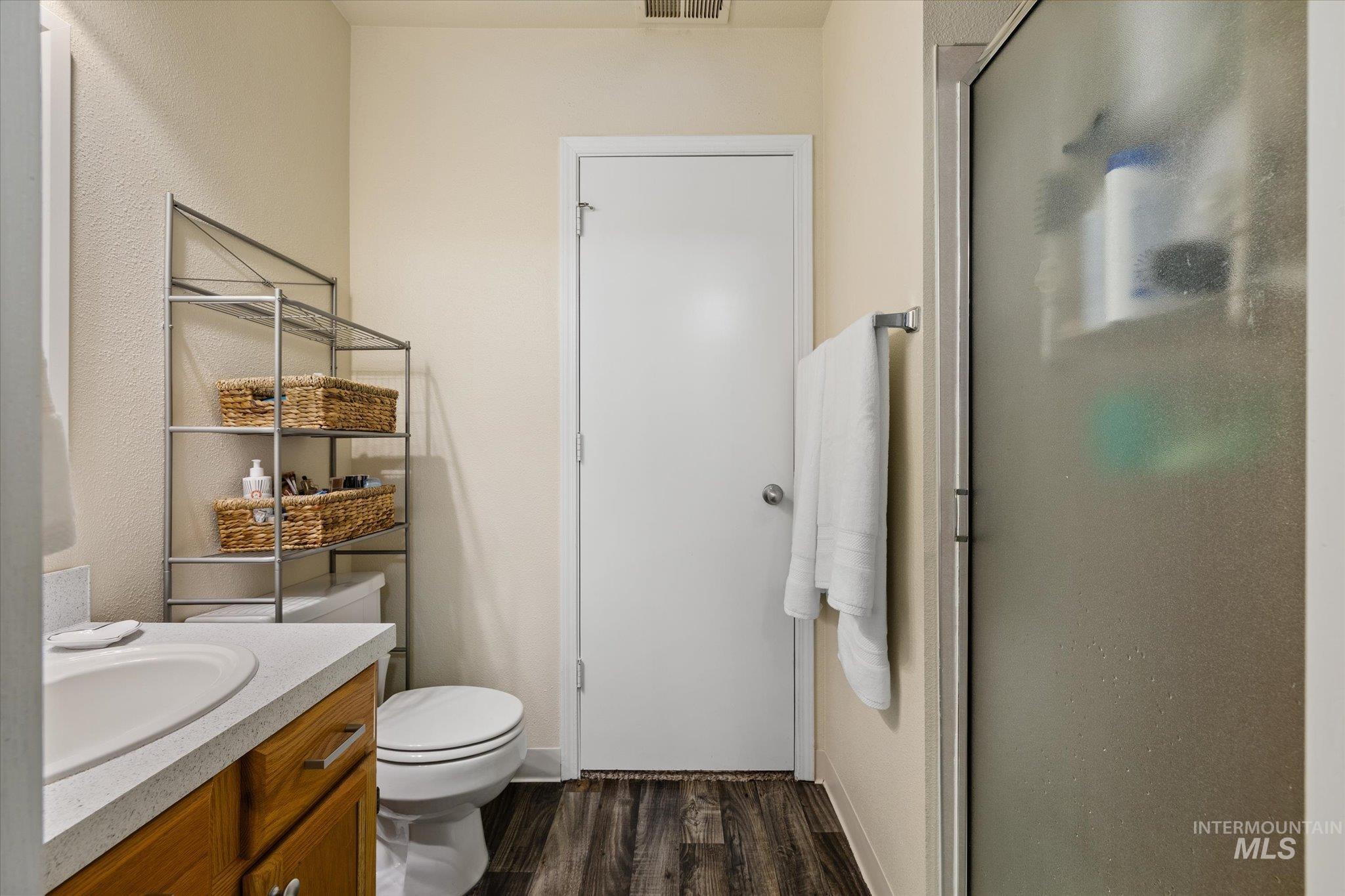 Full bathroom with a stall shower, vanity, dark wood finished floors, and a textured wall