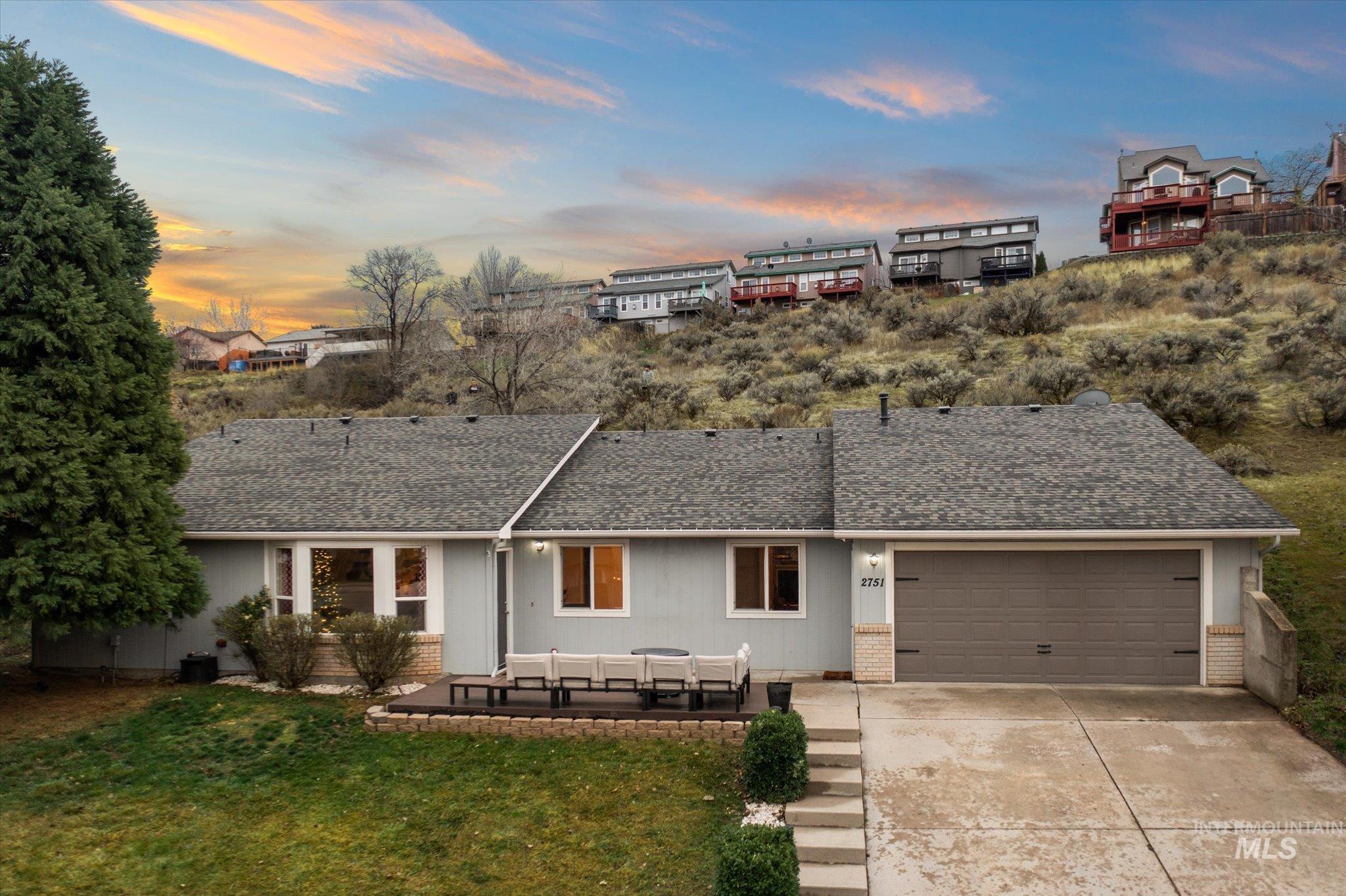 View of front of house with a shingled roof, concrete driveway, brick siding, a patio area, and a lawn