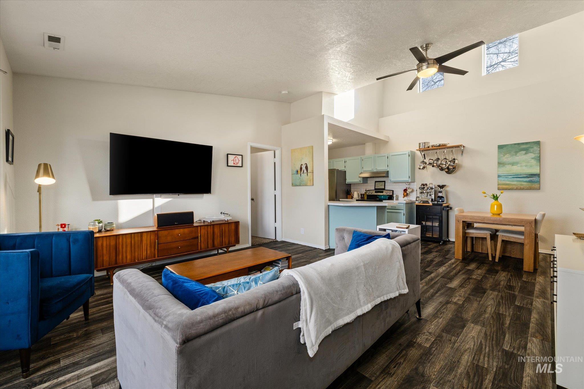 Living room with dark wood-style flooring, high vaulted ceiling, ceiling fan, and a textured ceiling