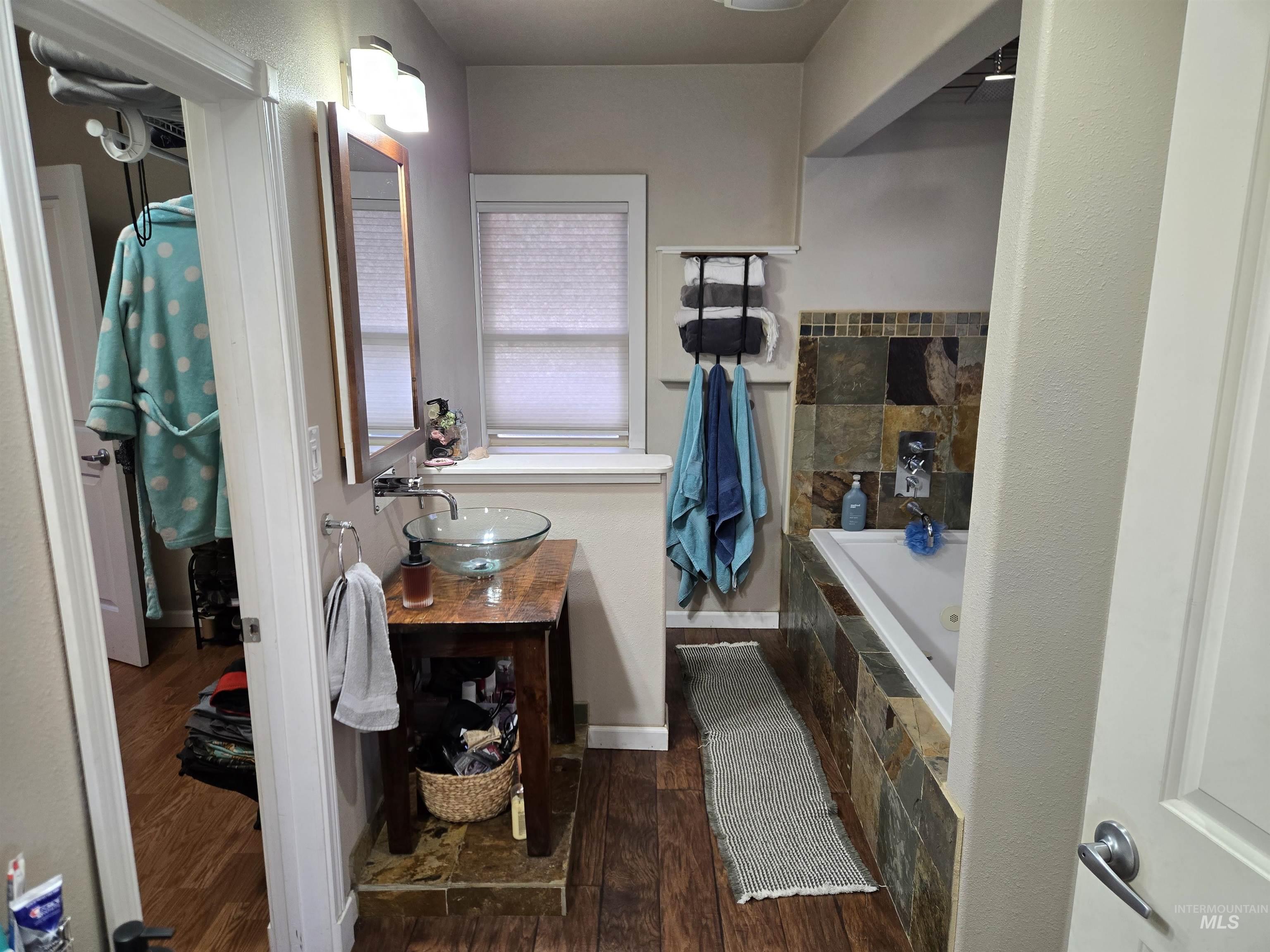 Bathroom featuring vanity, tiled bath, a walk in closet, and dark wood-type flooring