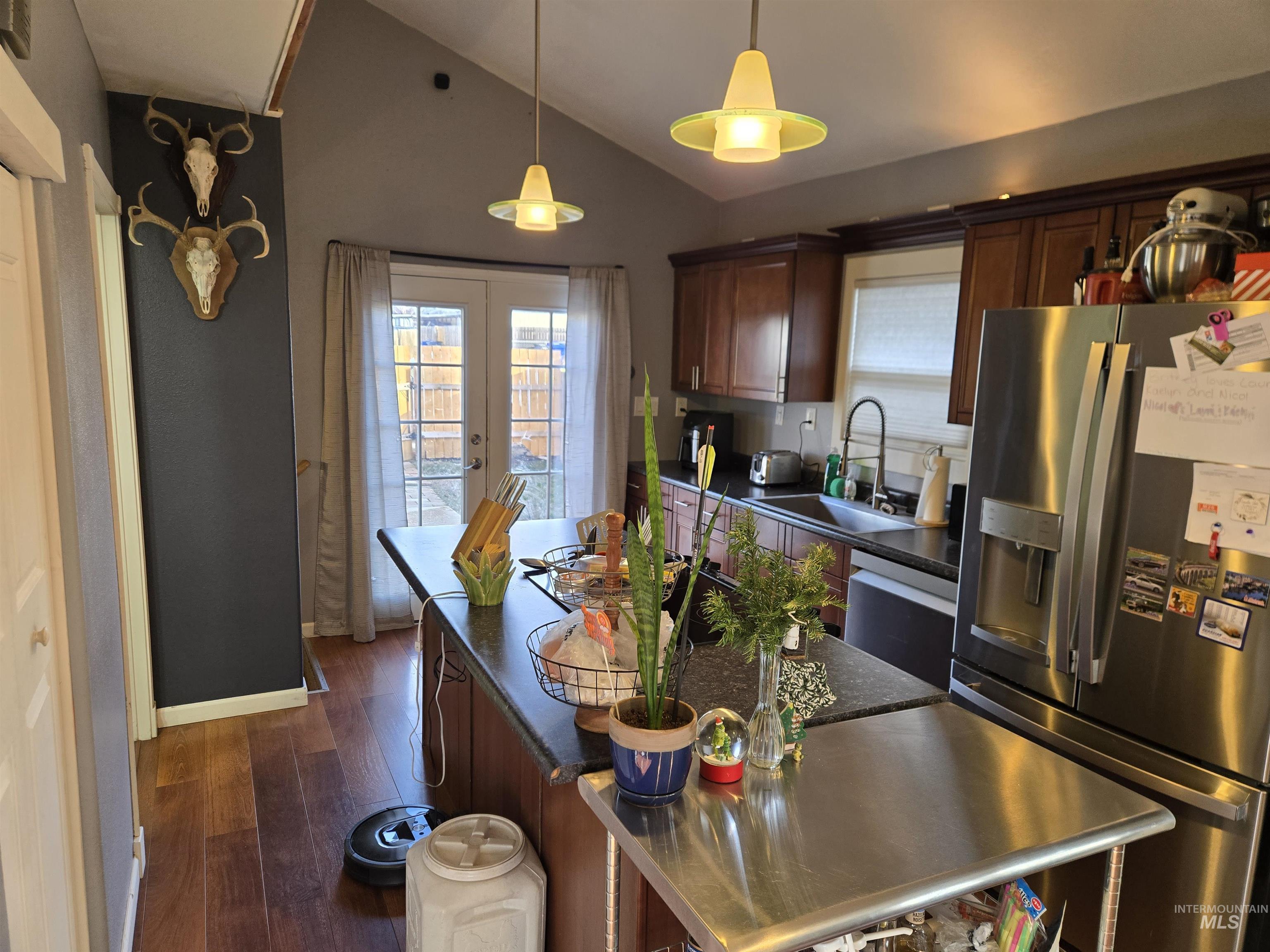 Kitchen with stainless steel appliances, vaulted ceiling, healthy amount of natural light, dark brown cabinets, and dark wood-style flooring