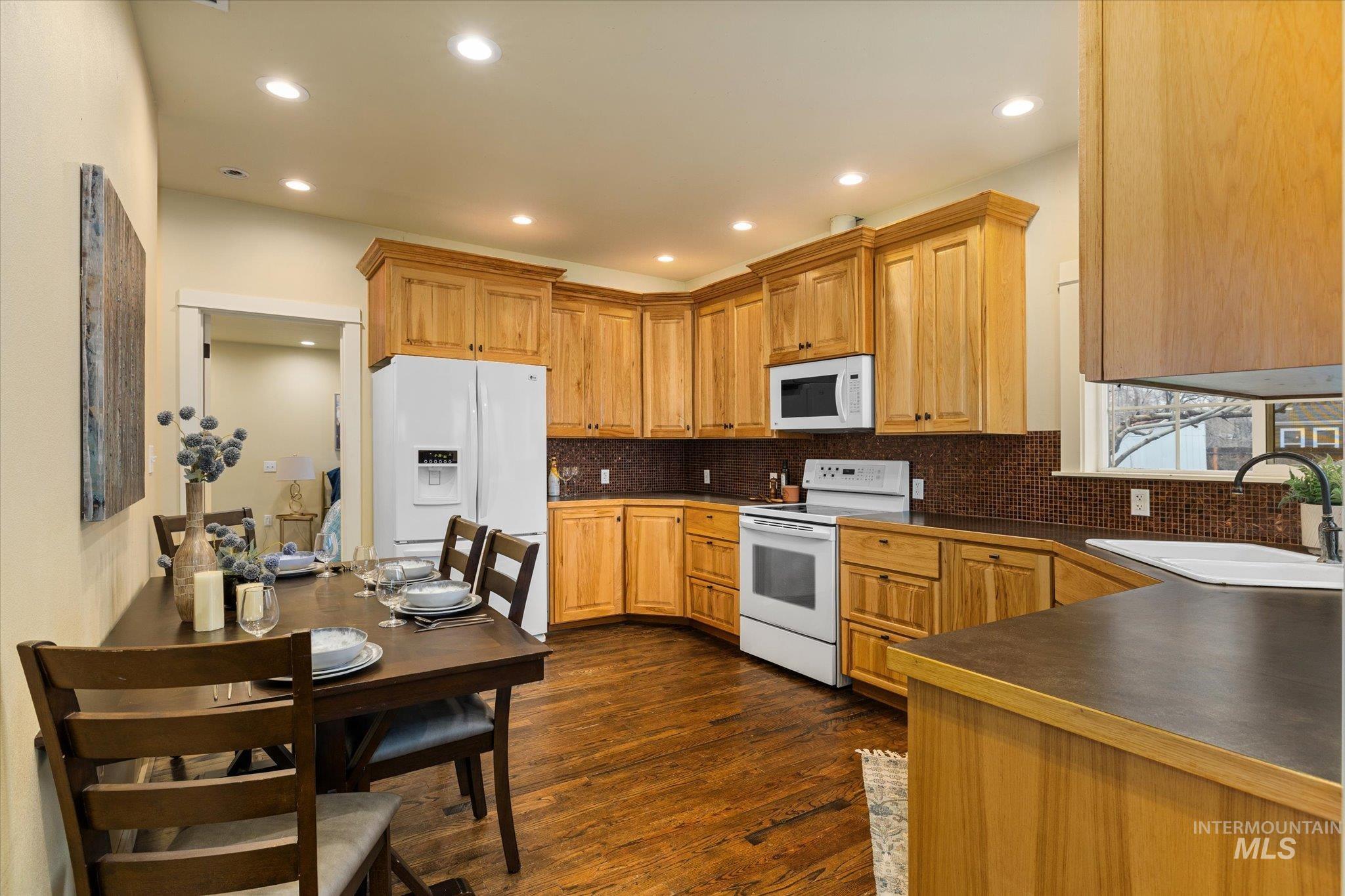 Kitchen featuring dark countertops, white appliances, dark wood-type flooring, tasteful backsplash, and recessed lighting
