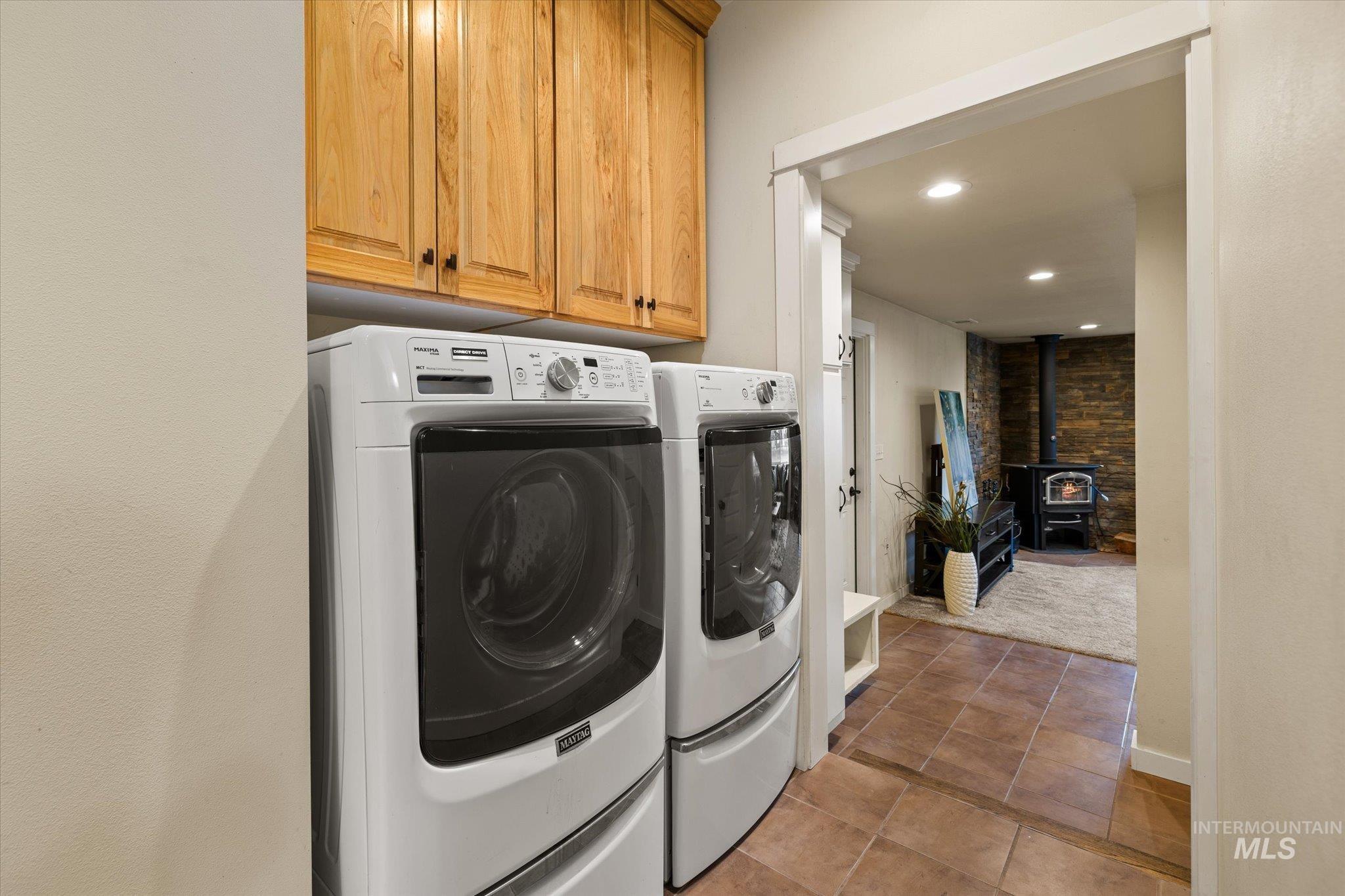 Laundry area with a wood stove, washer and clothes dryer, light tile patterned floors, cabinet space, and recessed lighting